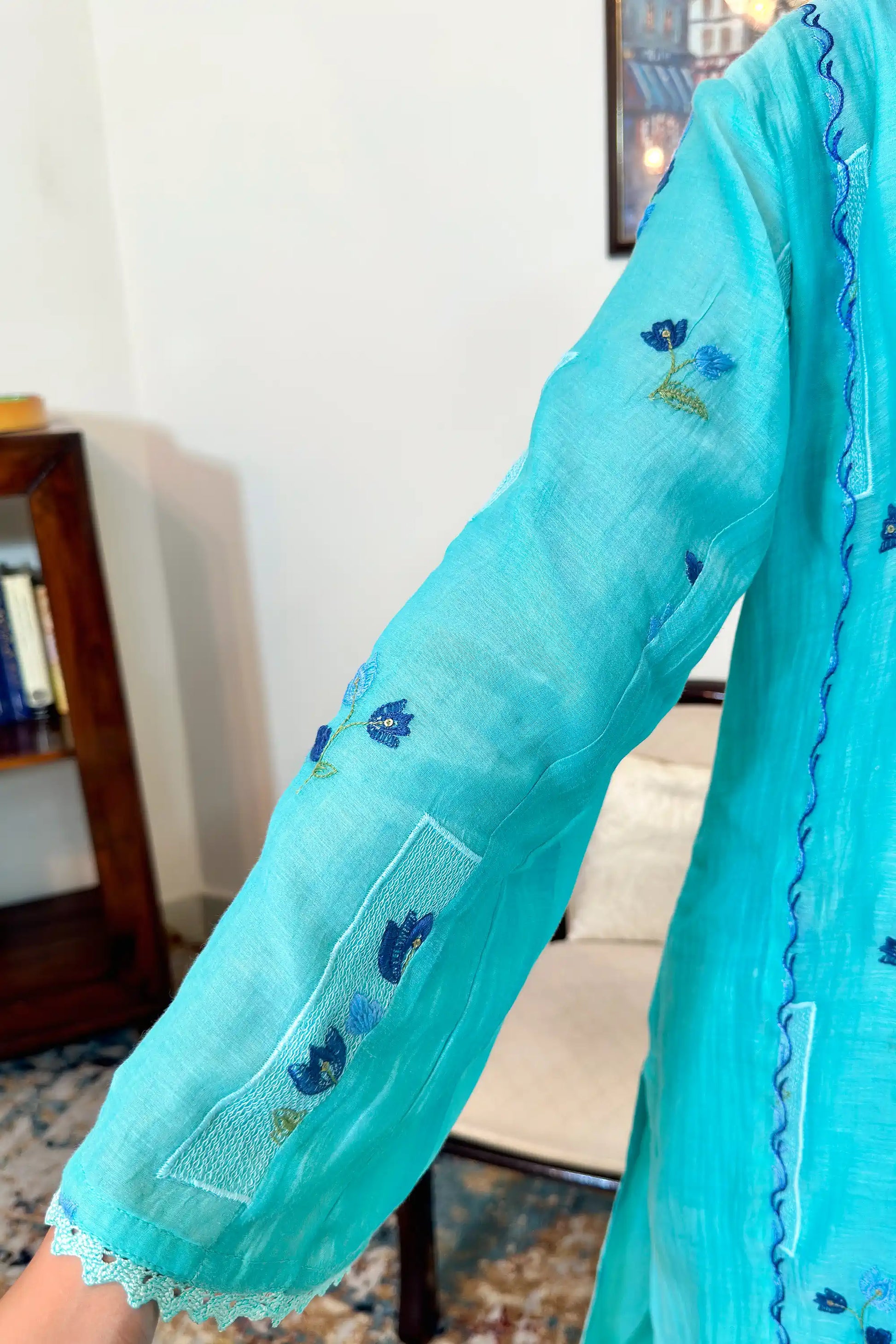 Close-up of the sleeve on an aqua-blue chanderi kurta, showing blue floral resham embroidery with a lace-trimmed cuff.