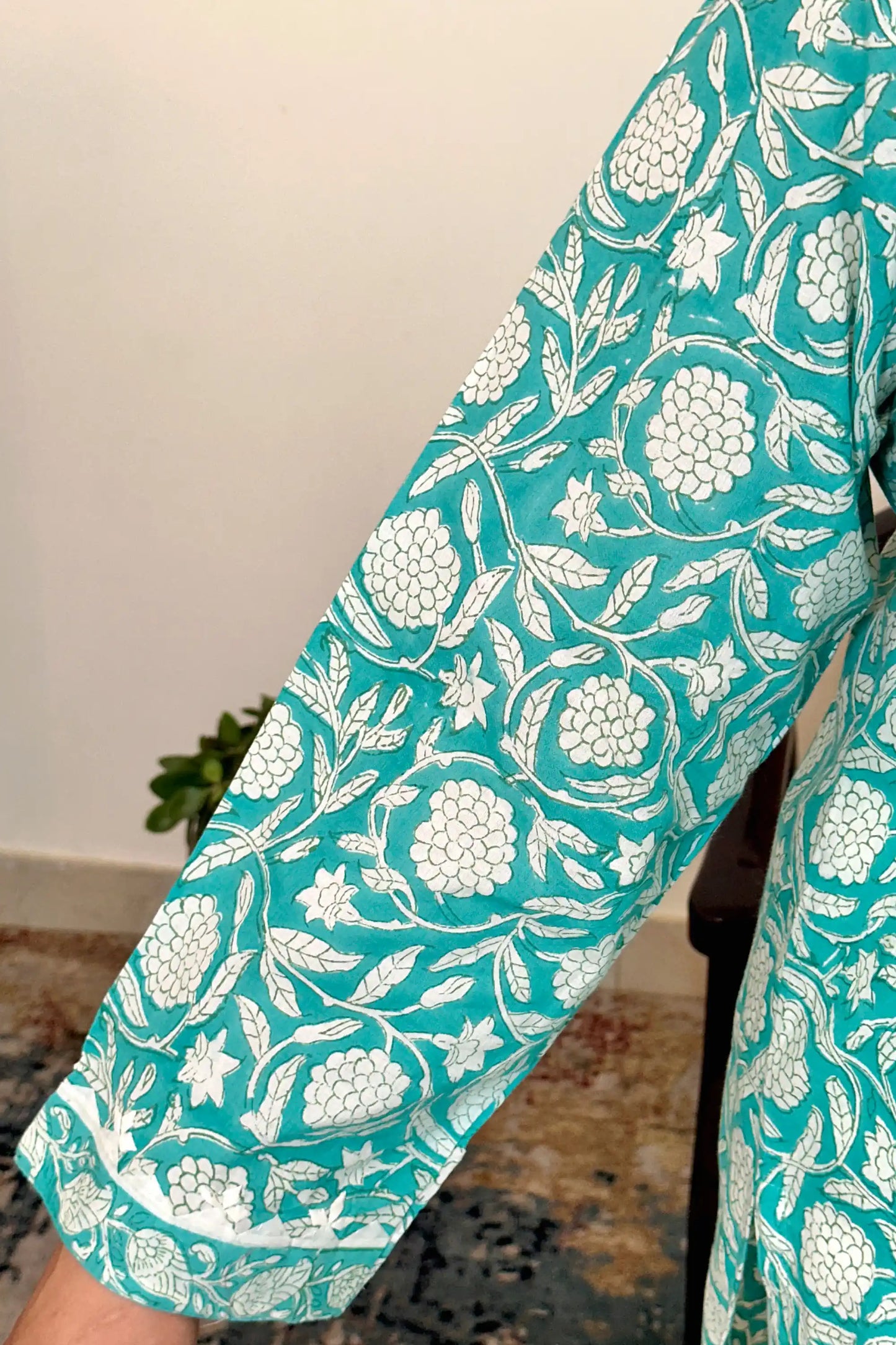 Close-up of the kurta sleeve showing the turquoise-green fabric with white floral print and applique bordered cuff.