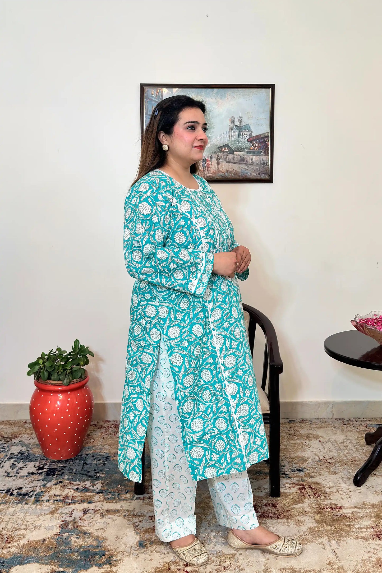 Side view of a woman wearing the turquoise-green printed kalidar kurta, paired with off-white printed trousers.