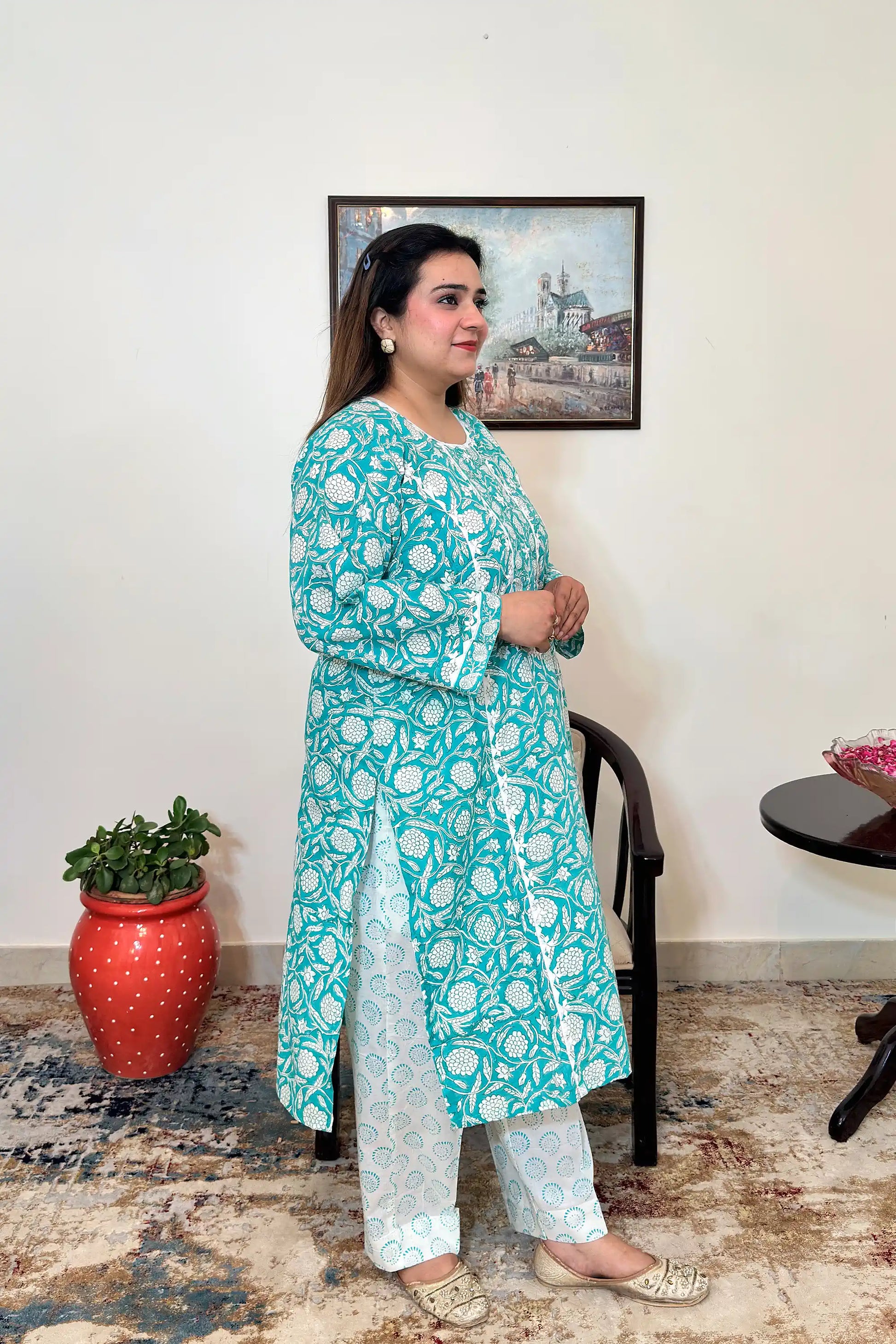 Side view of a woman wearing the turquoise-green printed kalidar kurta, paired with off-white printed trousers.