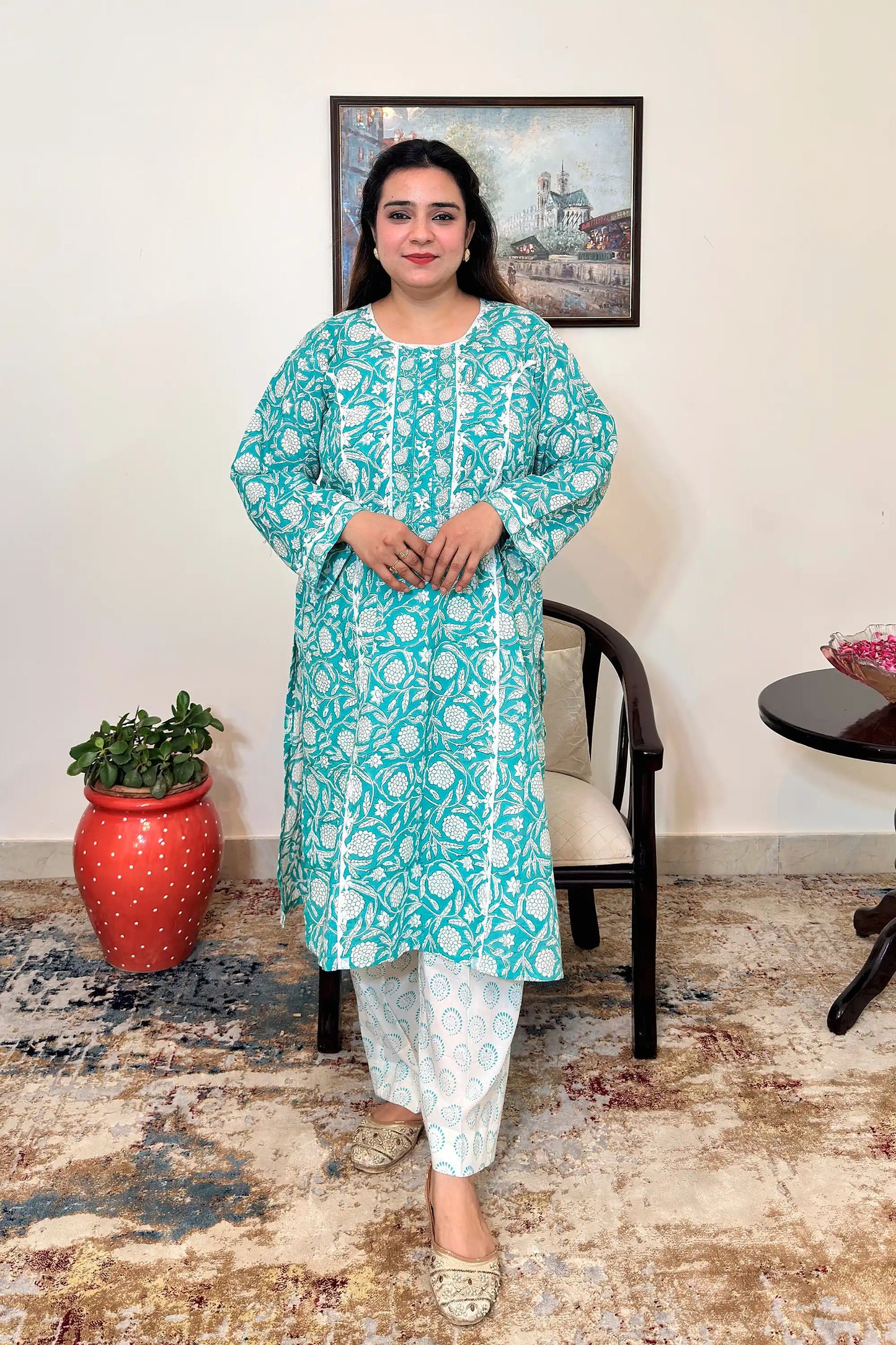 Front view of a woman wearing the turquoise-green mulmul cotton kalidar kurta with white floral print and off-white printed trousers.