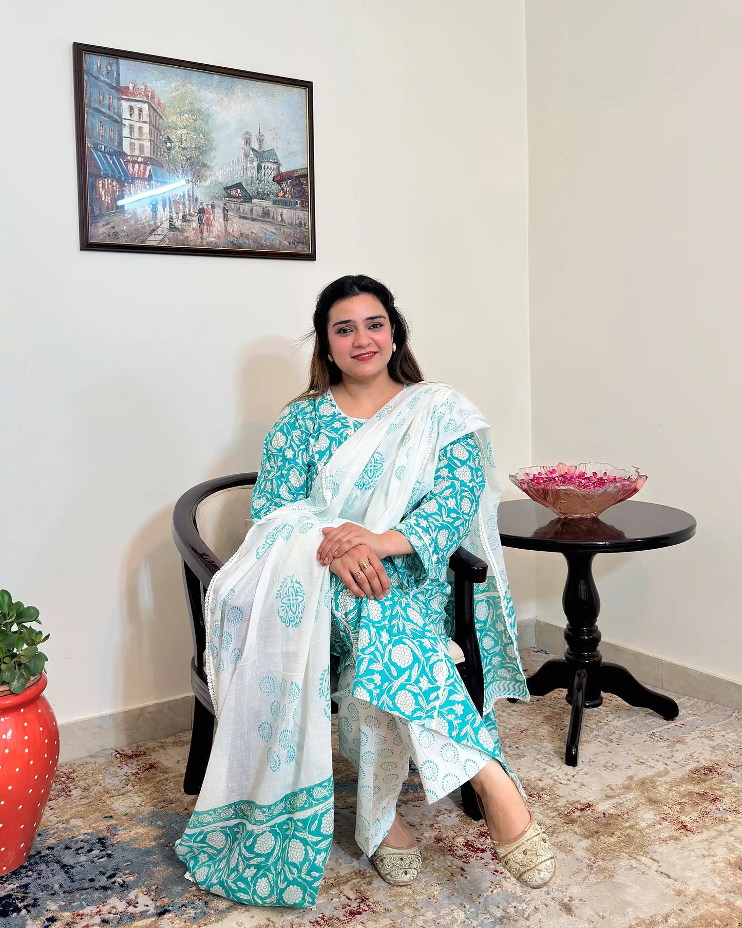 Front view of a woman sitting, wearing the turquoise-green printed applique work kalidar kurta with off-white printed dupatta and trousers.