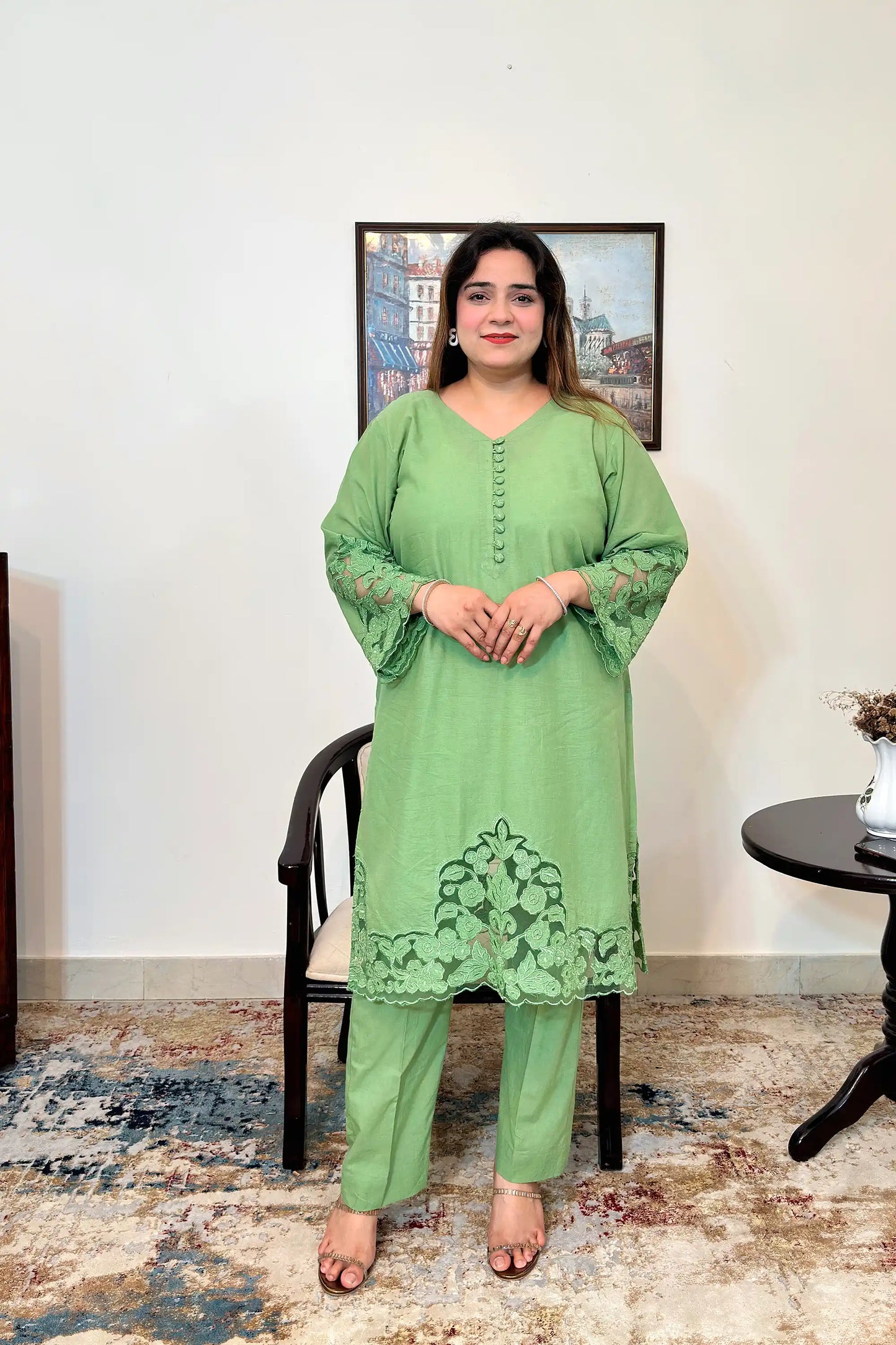 Front view of a green cotton straight kurta with fabric-covered buttons and floral cutwork sleeve cuffs and hem, paired with green trousers.