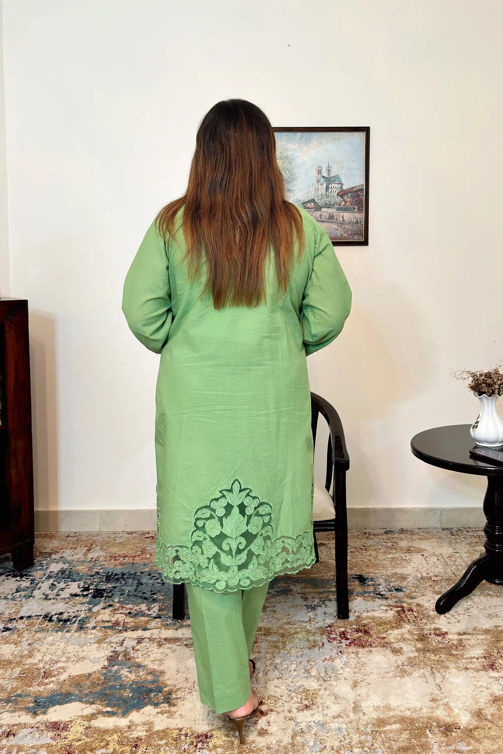 Back of a green cotton straight kurta with floral cutwork along the hem, model wearing green trousers.