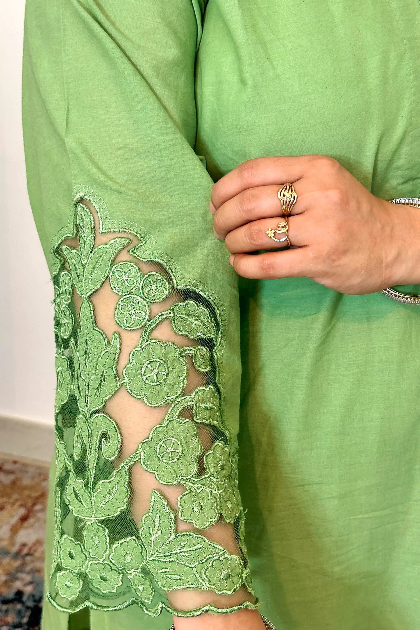 Close-up of the sleeve cuff showing floral cutwork with a vine and floral motif pattern on a sheer net base.