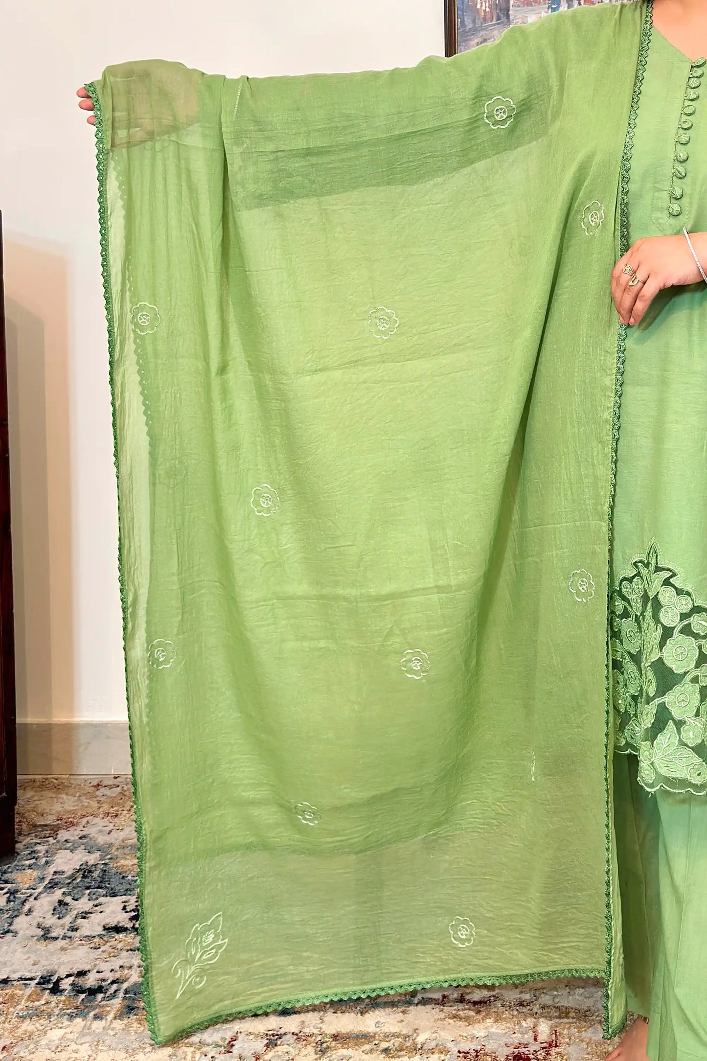 Close-up of the dupatta spread open, showing scattered small embroidered floral motifs across the green fabric, a larger floral motif in one corner, and a scalloped edge.