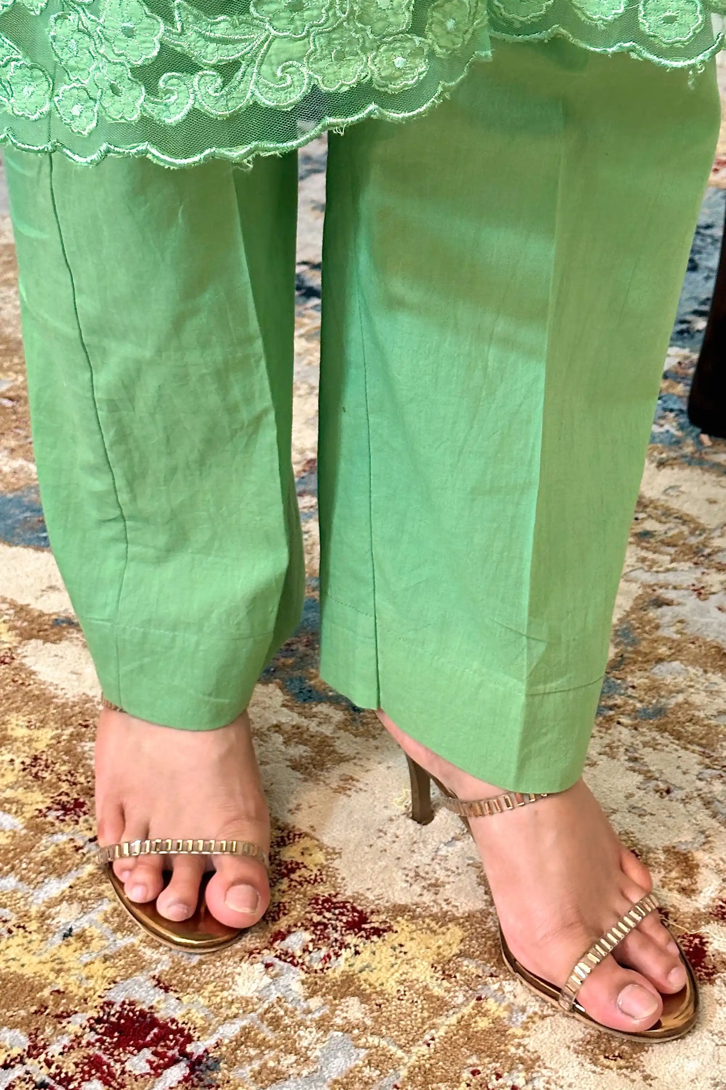 Close-up of the kurta hem showing floral cutwork along the scalloped edge, paired with green trousers.