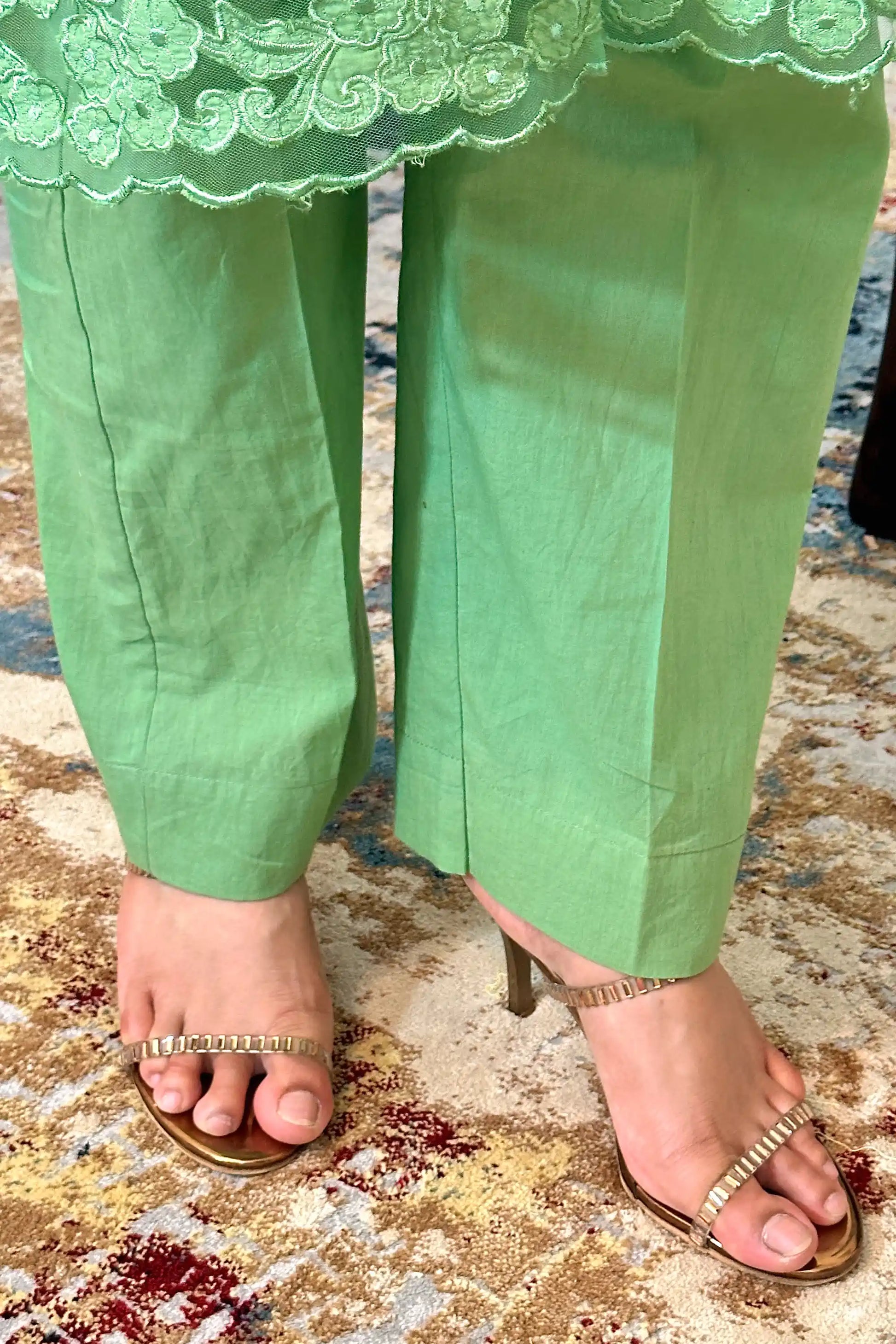 Close-up of the kurta hem showing floral cutwork along the scalloped edge, paired with green trousers.