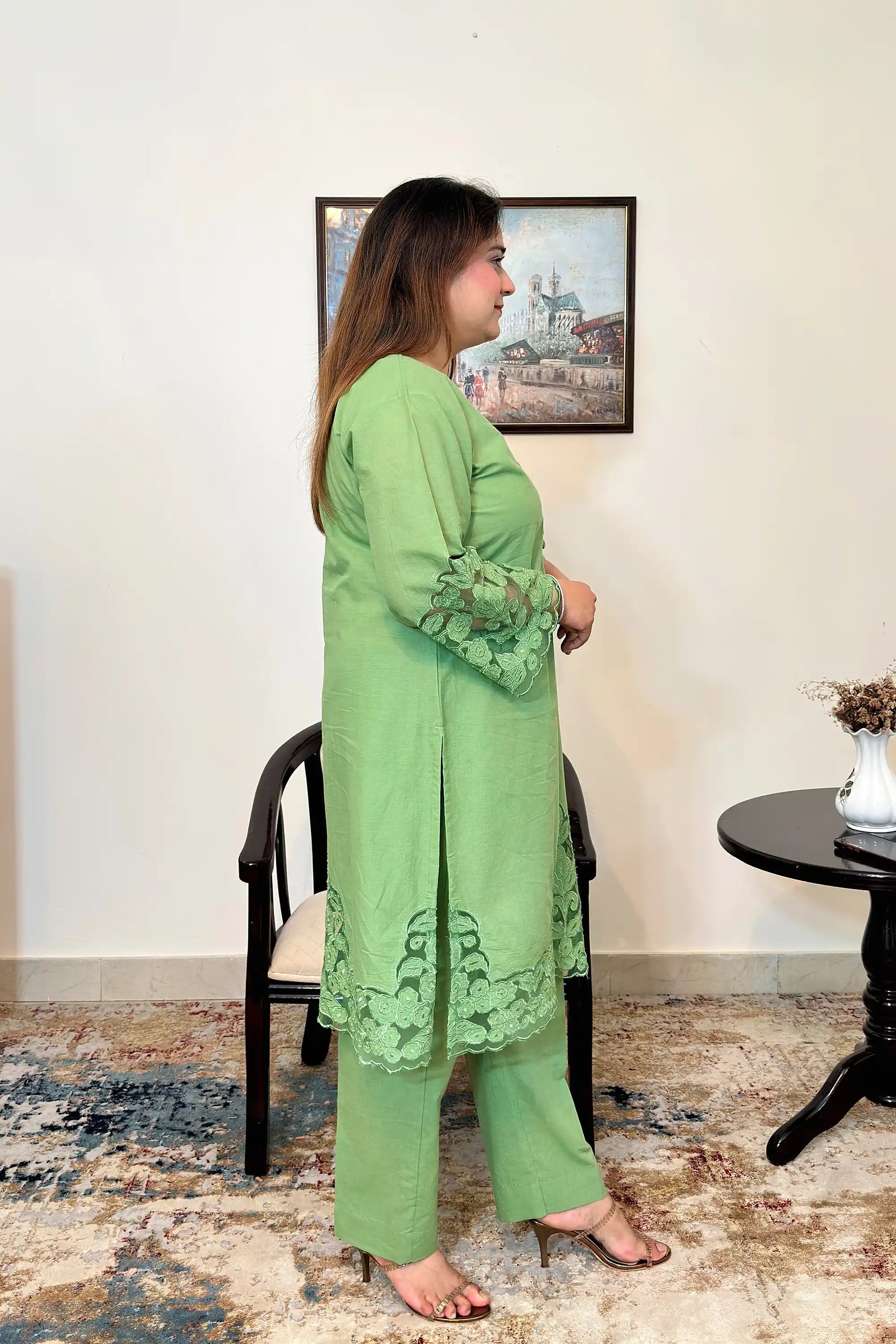 Model standing in a green cotton straight kurta with floral cutwork sleeve cuffs and hem, paired with green trousers.