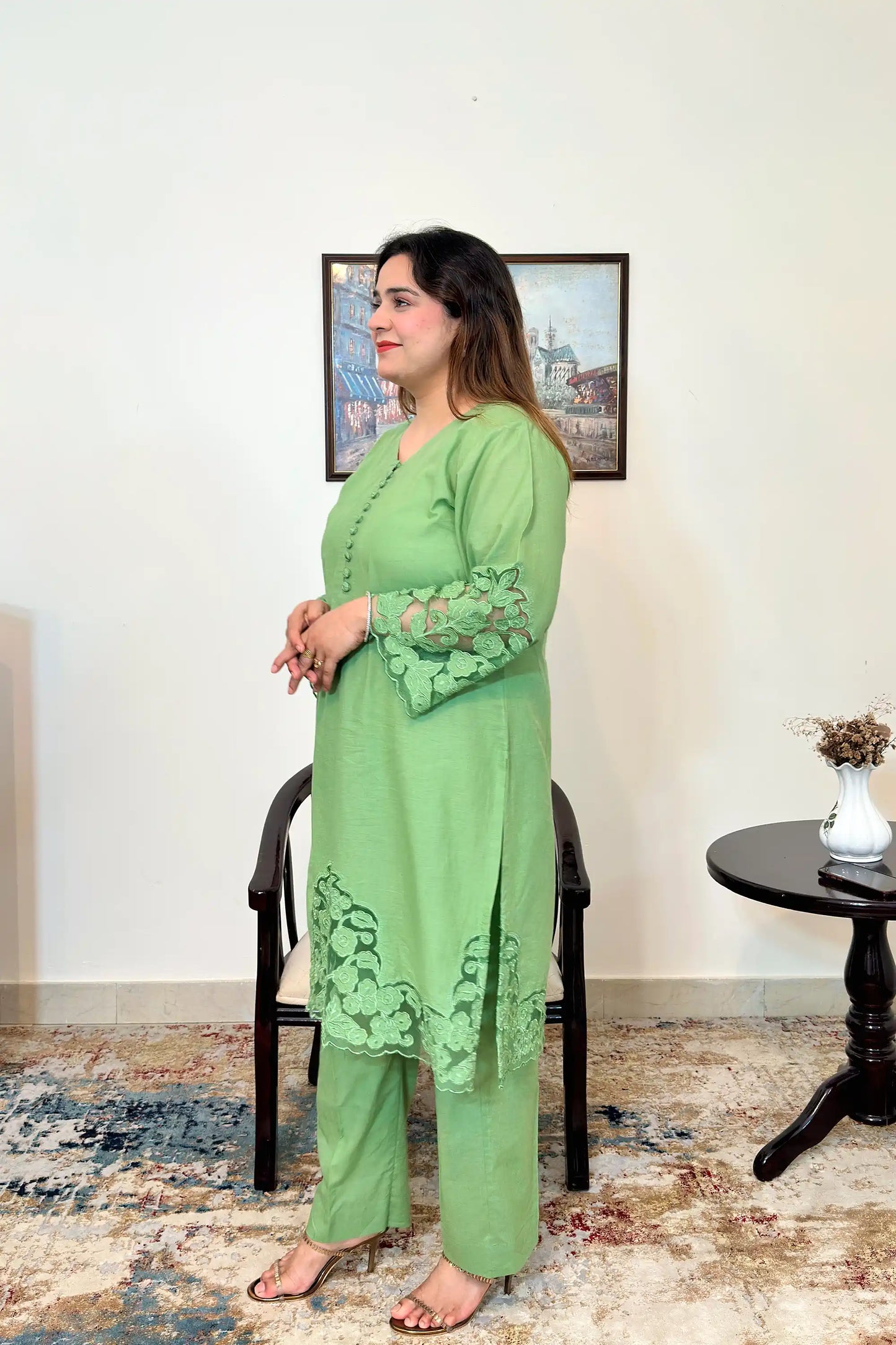 Side view of the model wearing a green cotton straight kurta with floral cutwork sleeve cuffs and hem, paired with green trousers.
