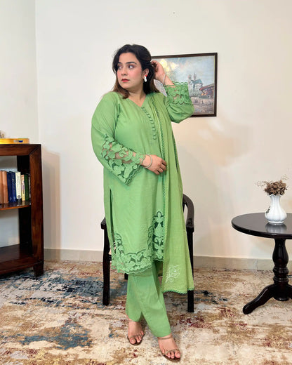 Model standing in a green cotton straight kurta with floral cutwork sleeve cuffs and hem, a green dupatta with scattered floral motifs and a scalloped edge, and green trousers, one hand raised to the hair.