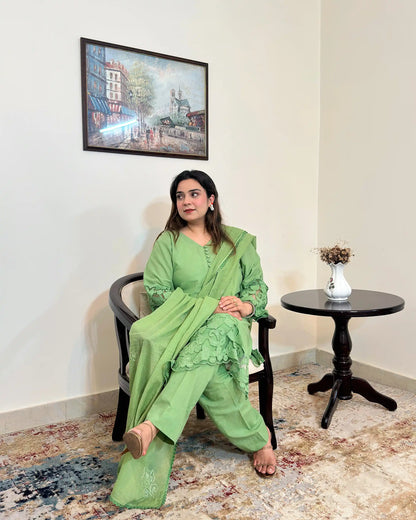 Model seated in a green cotton straight kurta with floral cutwork sleeve cuffs and hem, a green dupatta with scattered floral motifs and a scalloped edge, and green trousers, looking to the side.