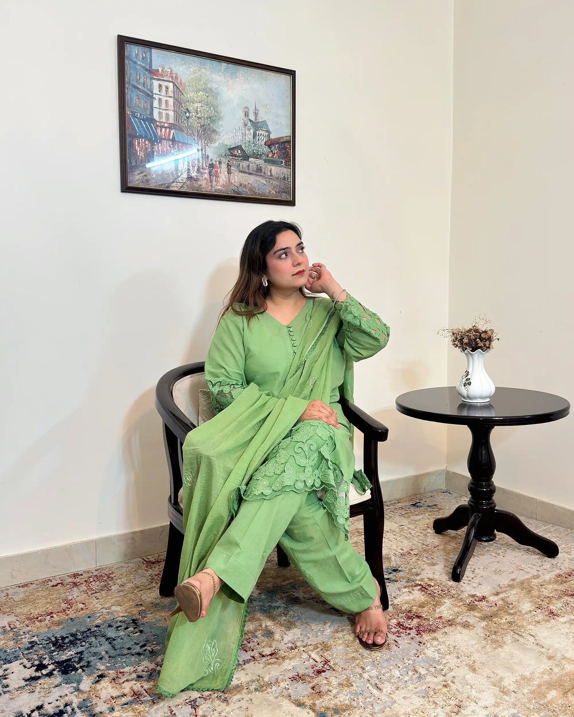 Model seated in a green cotton straight kurta with floral cutwork sleeve cuffs and hem, a green dupatta with scattered floral motifs and a scalloped edge, and green trousers, one hand resting near the face.