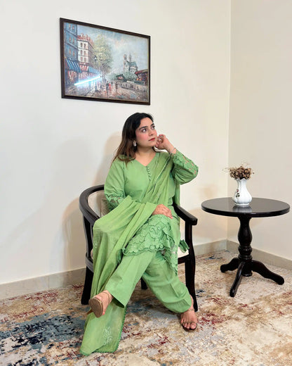 Model seated in a green cotton straight kurta with floral cutwork sleeve cuffs and hem, a green dupatta with scattered floral motifs and a scalloped edge, and green trousers, one hand resting near the face.