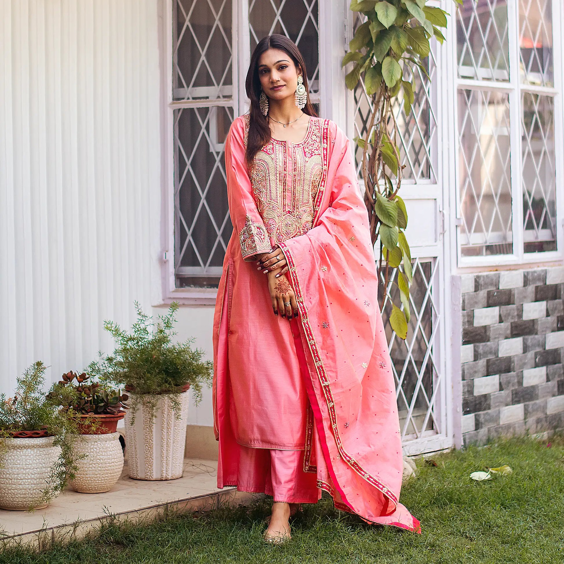 Indian woman in a peach chanderi kurta set featuring intricate zardozi embroidery, holding a peach dupatta and wearing a matching palazzo.