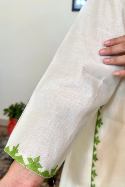 Close-up of the sleeve cuff, showing a green appliqué leaf trim along the hem.