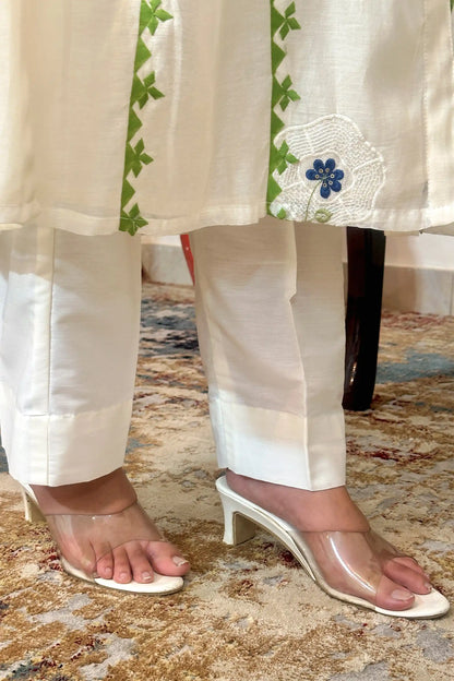 Close-up of the kurta hem meeting the off-white trousers, showing the green appliqué vine trim and a white circular embroidered motif with a blue flower near the hem.