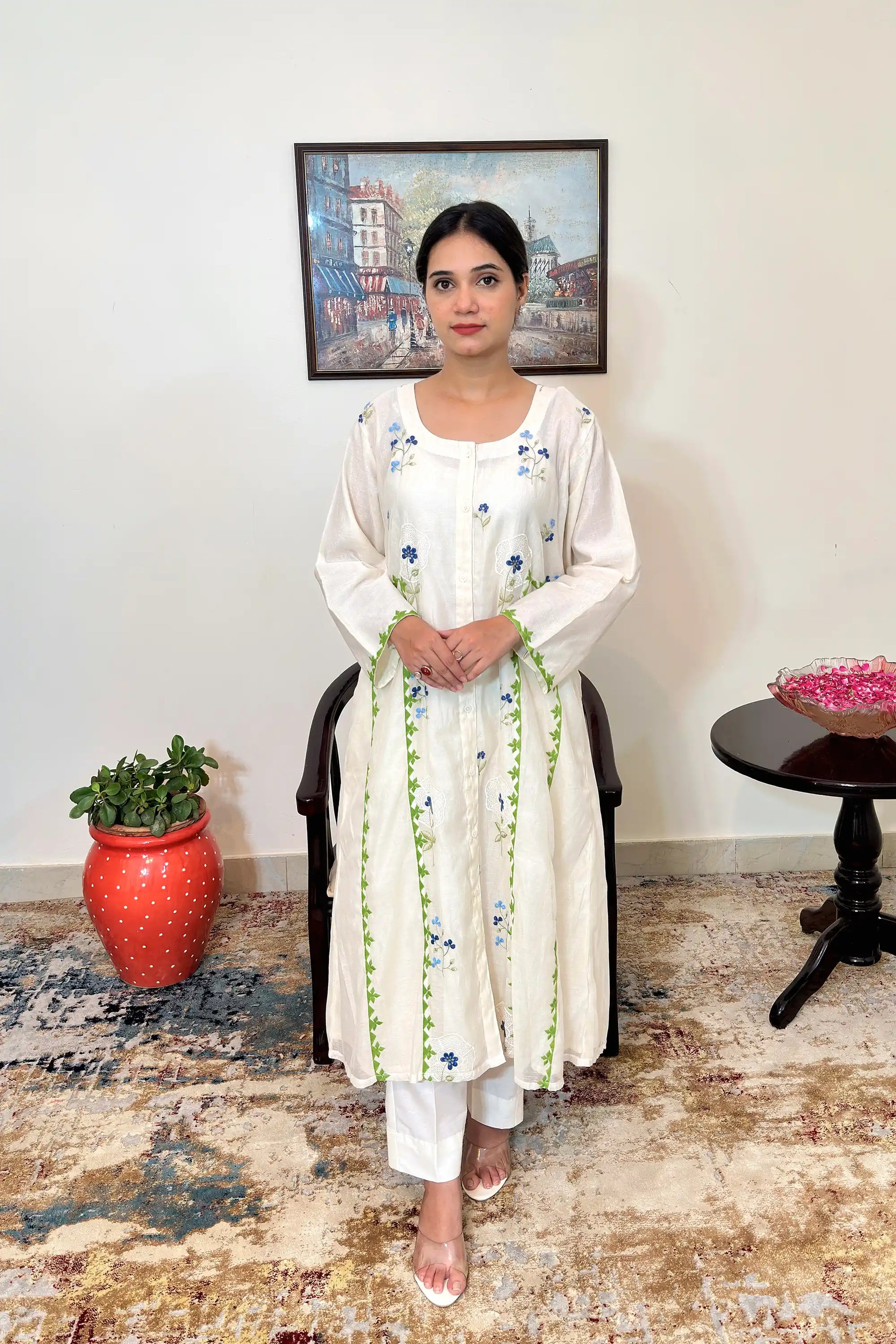 Front view of the off-white chanderi A-line kurta and off-white trousers, showing the flared silhouette at the hem along with scattered blue floral embroidery and green appliqué vine trim.