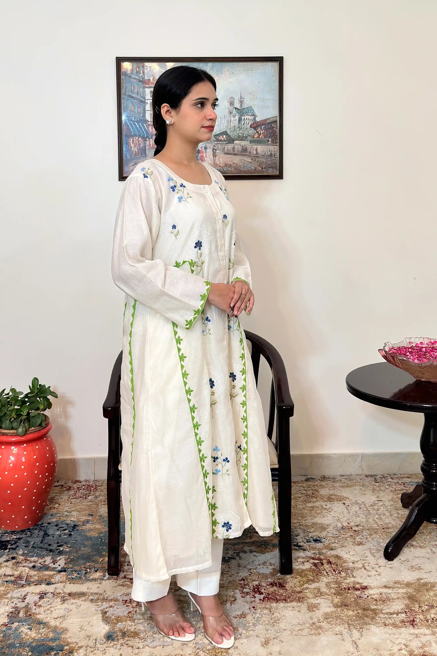 Right side view of the model wearing the off-white chanderi A-line kurta, showing the green appliqué vine trim along the front seam and blue floral embroidery across the bodice.