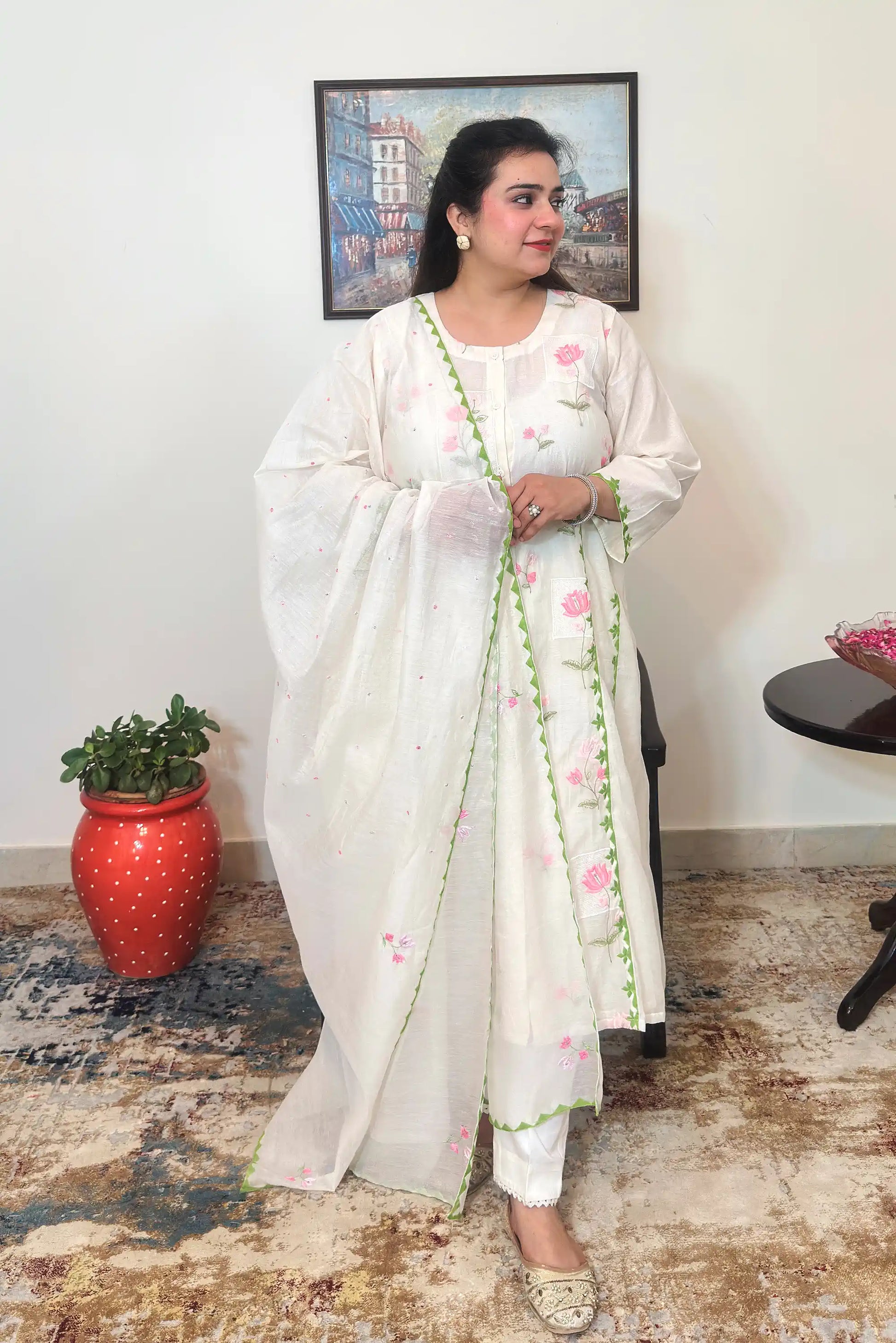 Front view of an off-white chanderi A-line kurta with pink floral embroidery and green applique vine trim, worn with an off-white dupatta and off-white trousers.