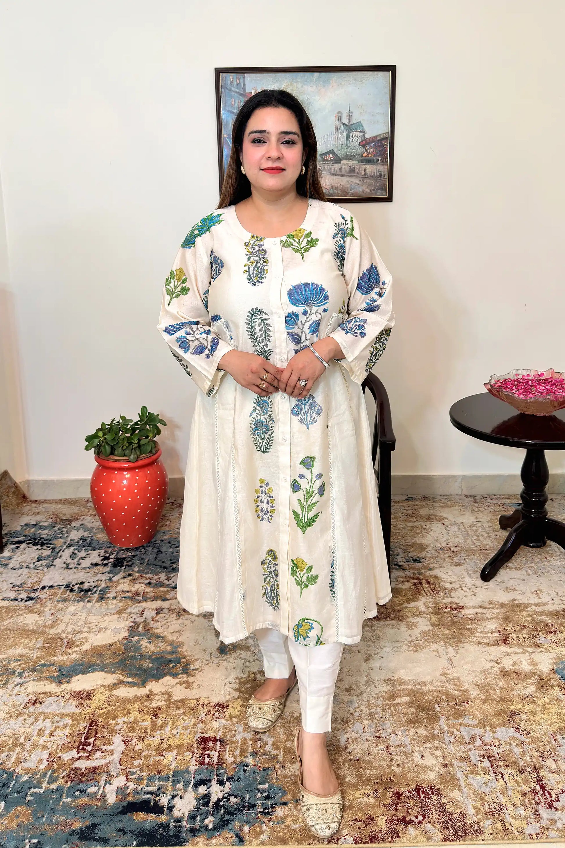 Front view of an off-white chanderi A-line kurta with blue-green floral mughal print and off-white trousers.