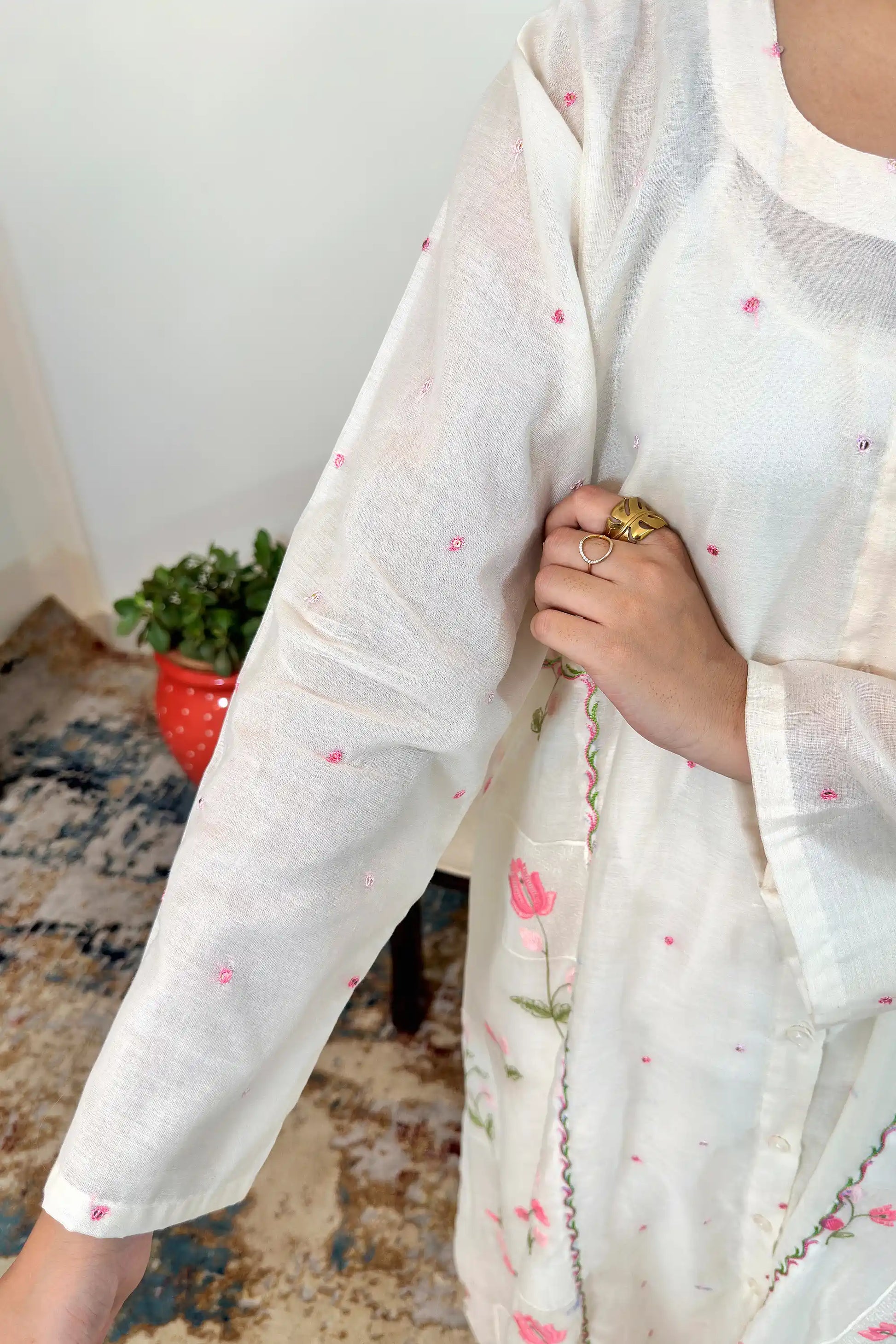 Close-up of the sleeve and front panel of the off-white chanderi kurta showing pink resham embroidery, held by hand.