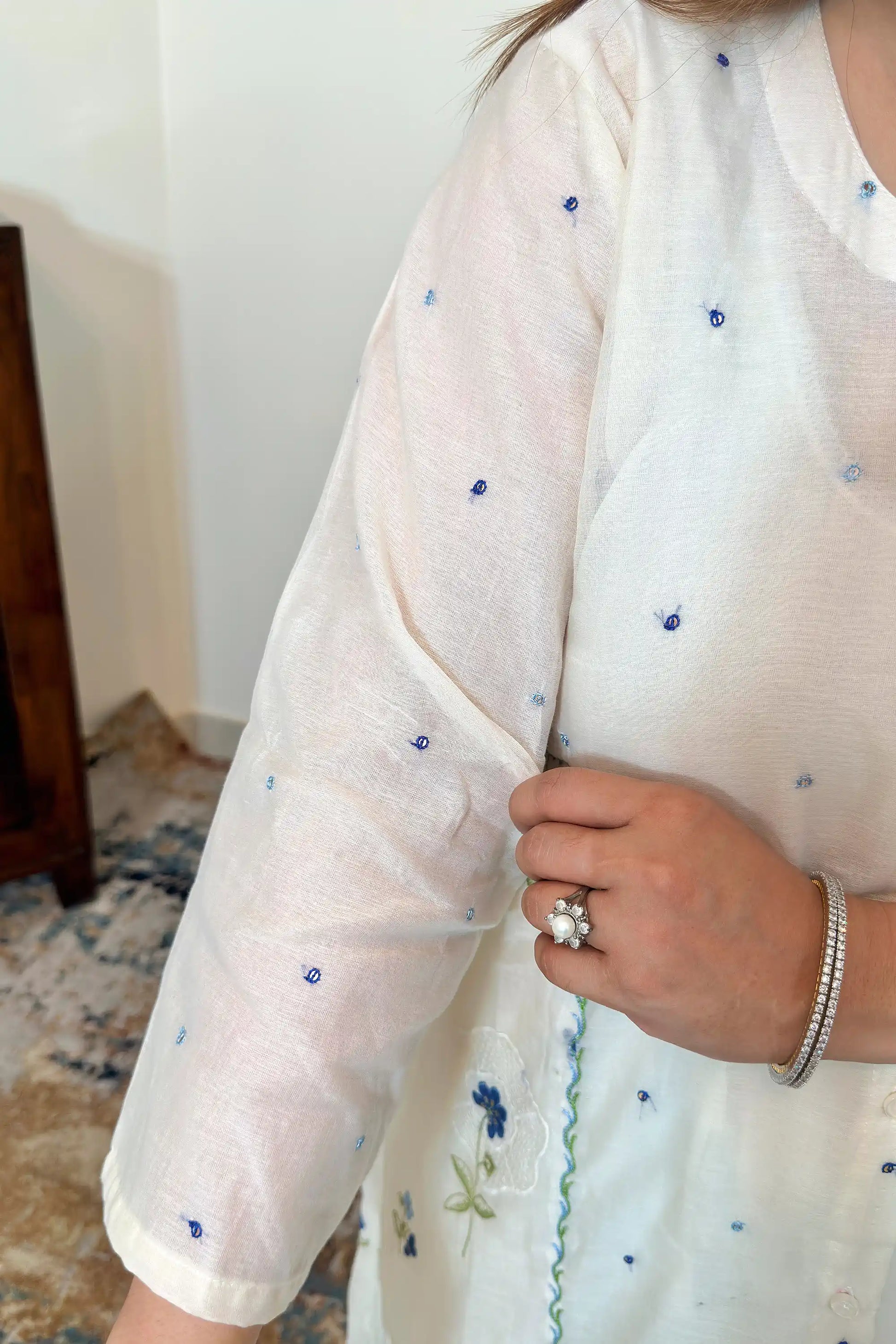 Close-up of the sleeve of an off-white chanderi kurta with scattered blue resham embroidery.
