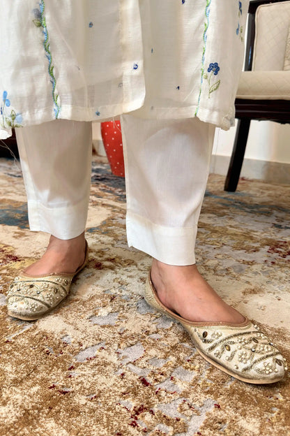 Close-up of the hem of an off-white chanderi kurta with blue floral resham embroidery, paired with off-white trousers.