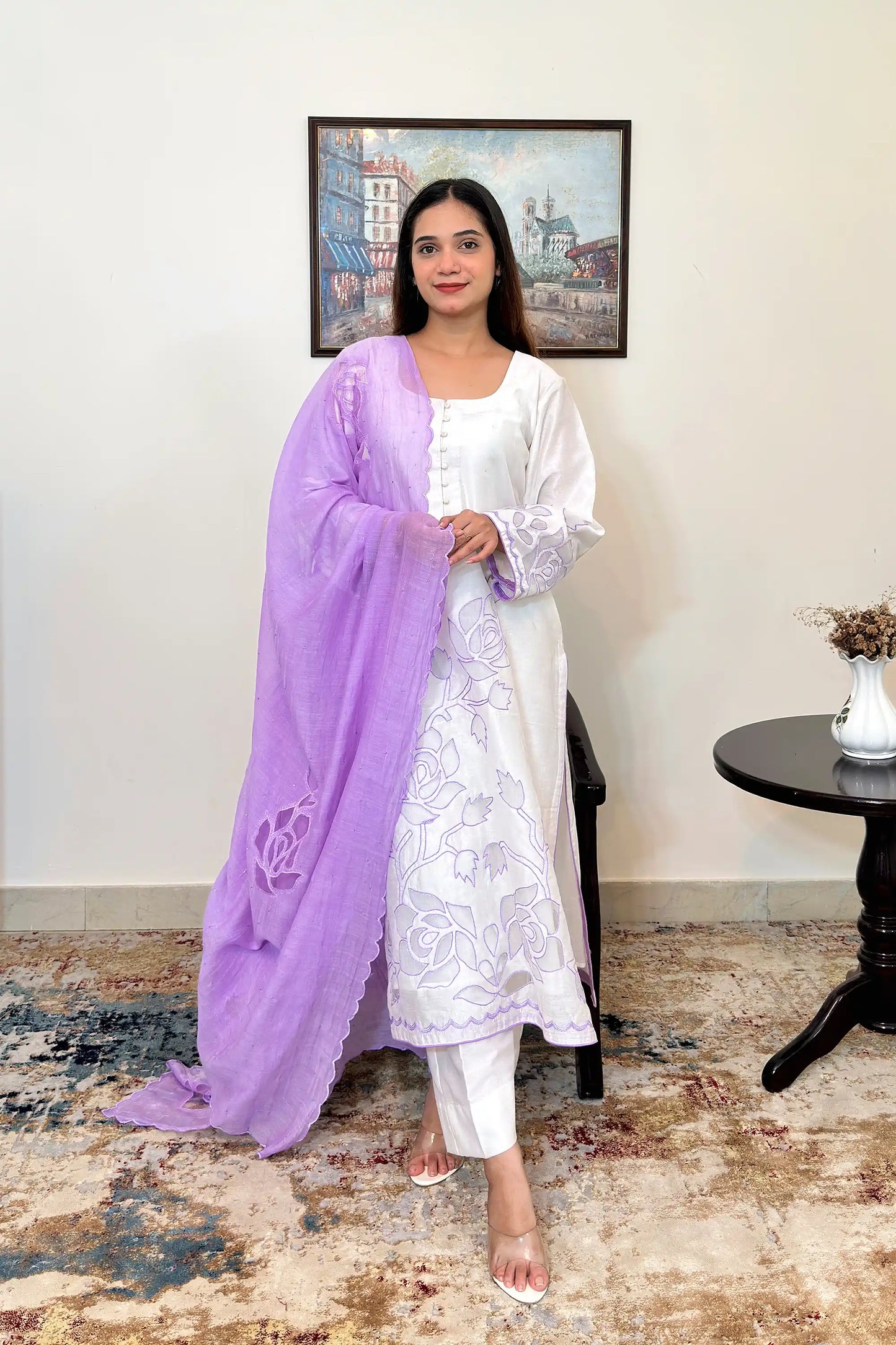 Front view of a woman wearing an off-white chanderi straight kurta with floral cutwork embroidery on the sleeves and hem, paired with a purple chanderi dupatta with floral cutwork and off-white trousers, dupatta on.
