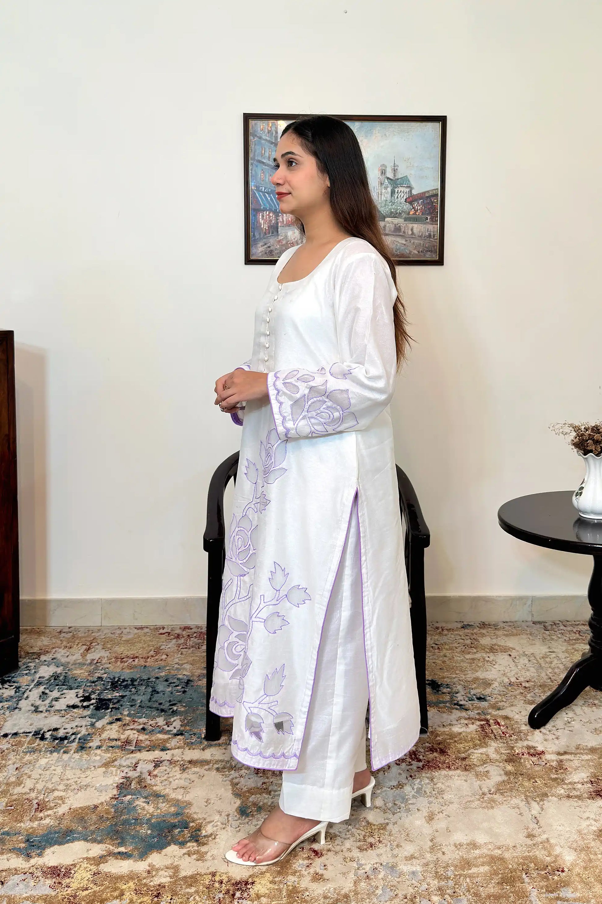 Side view of the off-white chanderi straight kurta with floral cutwork embroidery on the sleeves and hem, paired with off-white trousers.