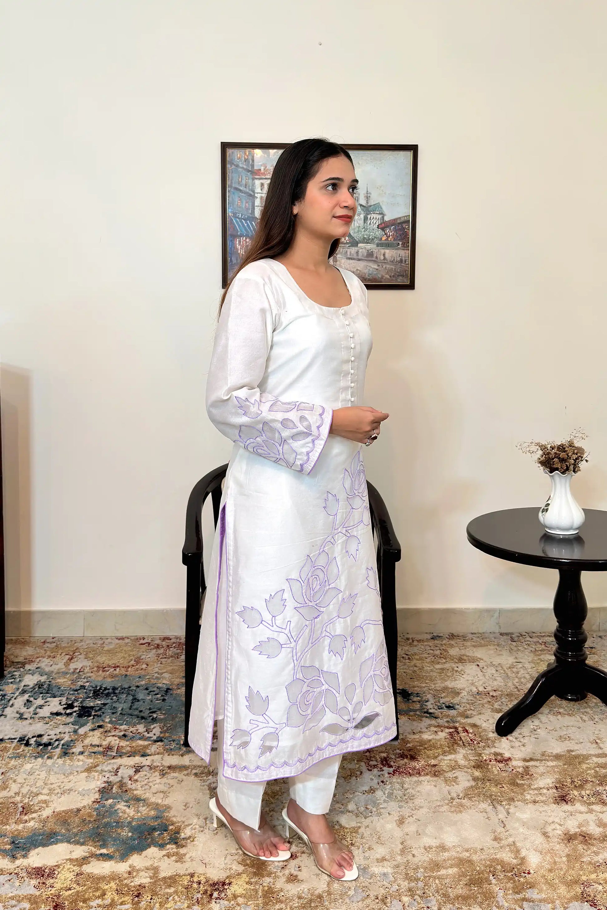 Side view of the off-white chanderi straight kurta with floral cutwork embroidery on the sleeves and hem, paired with off-white trousers.