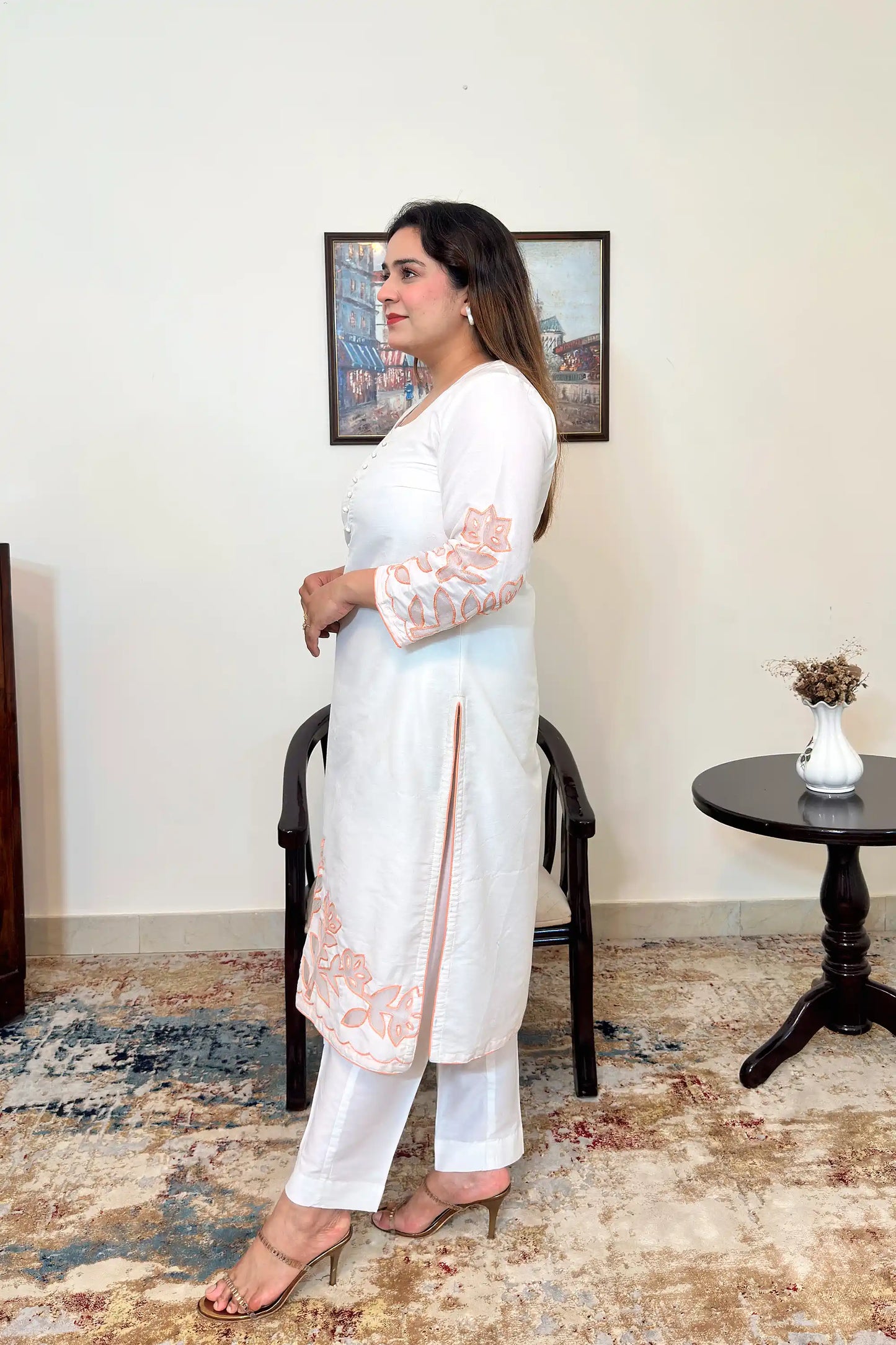 Side view of the off-white chanderi straight kurta with floral cutwork on the sleeve and hem, worn with off-white trousers.