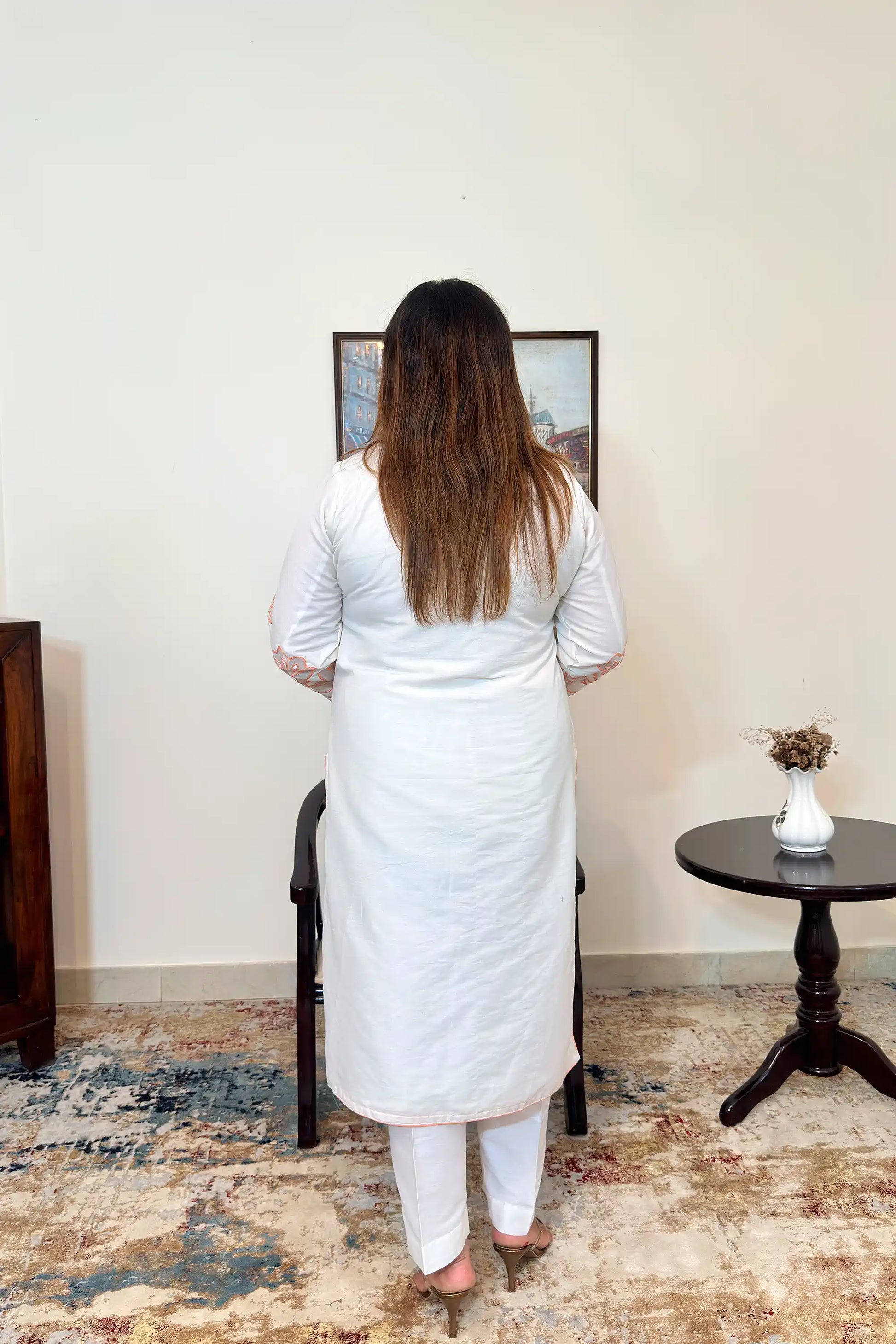 Back view of the off-white chanderi straight kurta with floral cutwork on the sleeves, worn with off-white trousers.