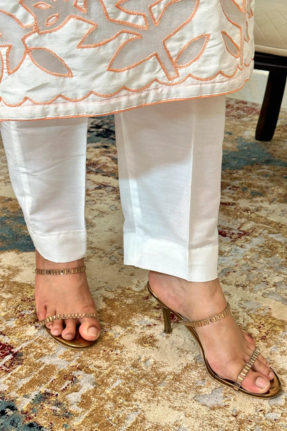 Close-up of the hem of the off-white chanderi kurta with floral cutwork, worn over off-white trousers.