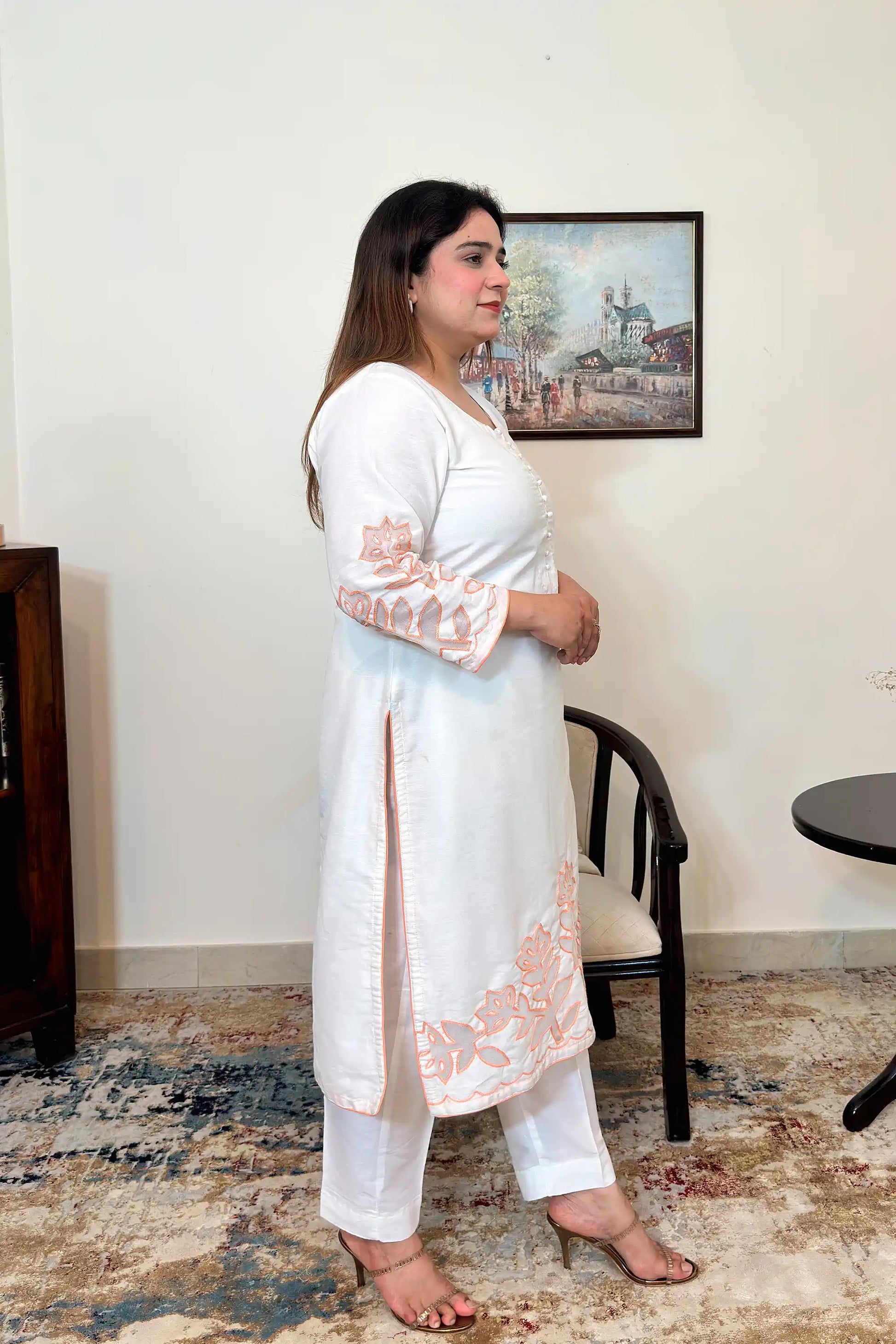 Side view of the off-white chanderi straight kurta with floral cutwork on the sleeve and hem, worn with off-white trousers.