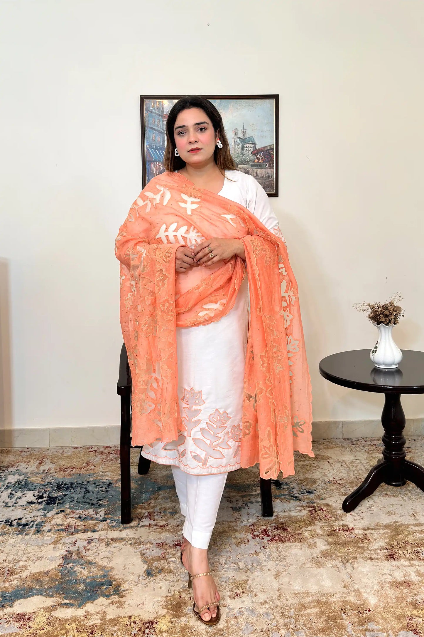 Front view of the off-white chanderi straight kurta with floral cutwork on the hem, worn with a peach dupatta featuring floral cutwork, and off-white trousers.