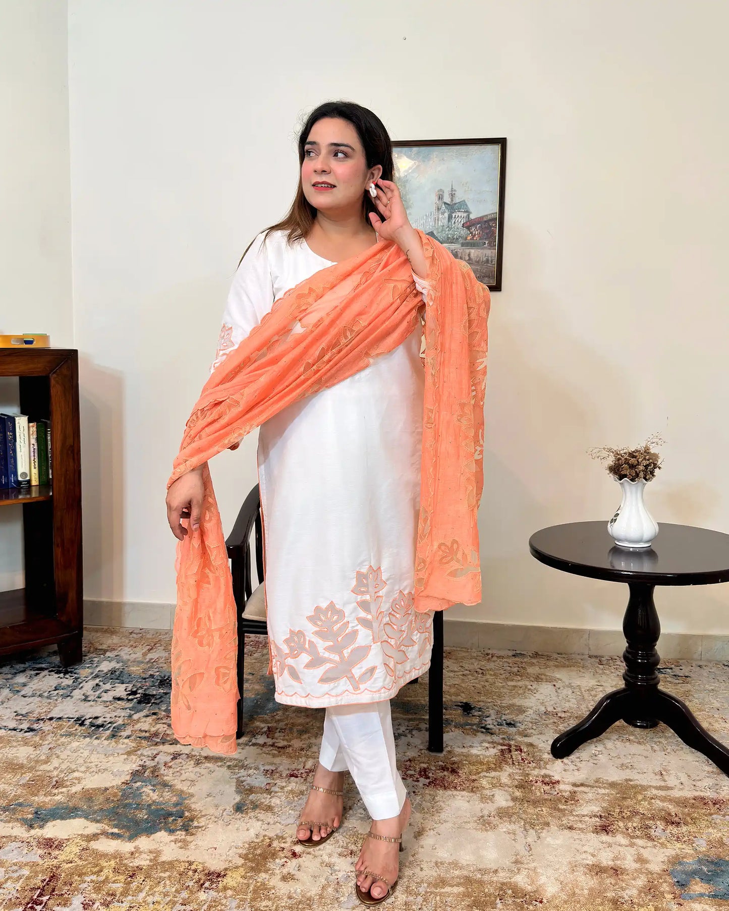 Front view of the off-white chanderi straight kurta with floral cutwork on the sleeve and hem, worn with a peach dupatta featuring floral cutwork, and off-white trousers.
