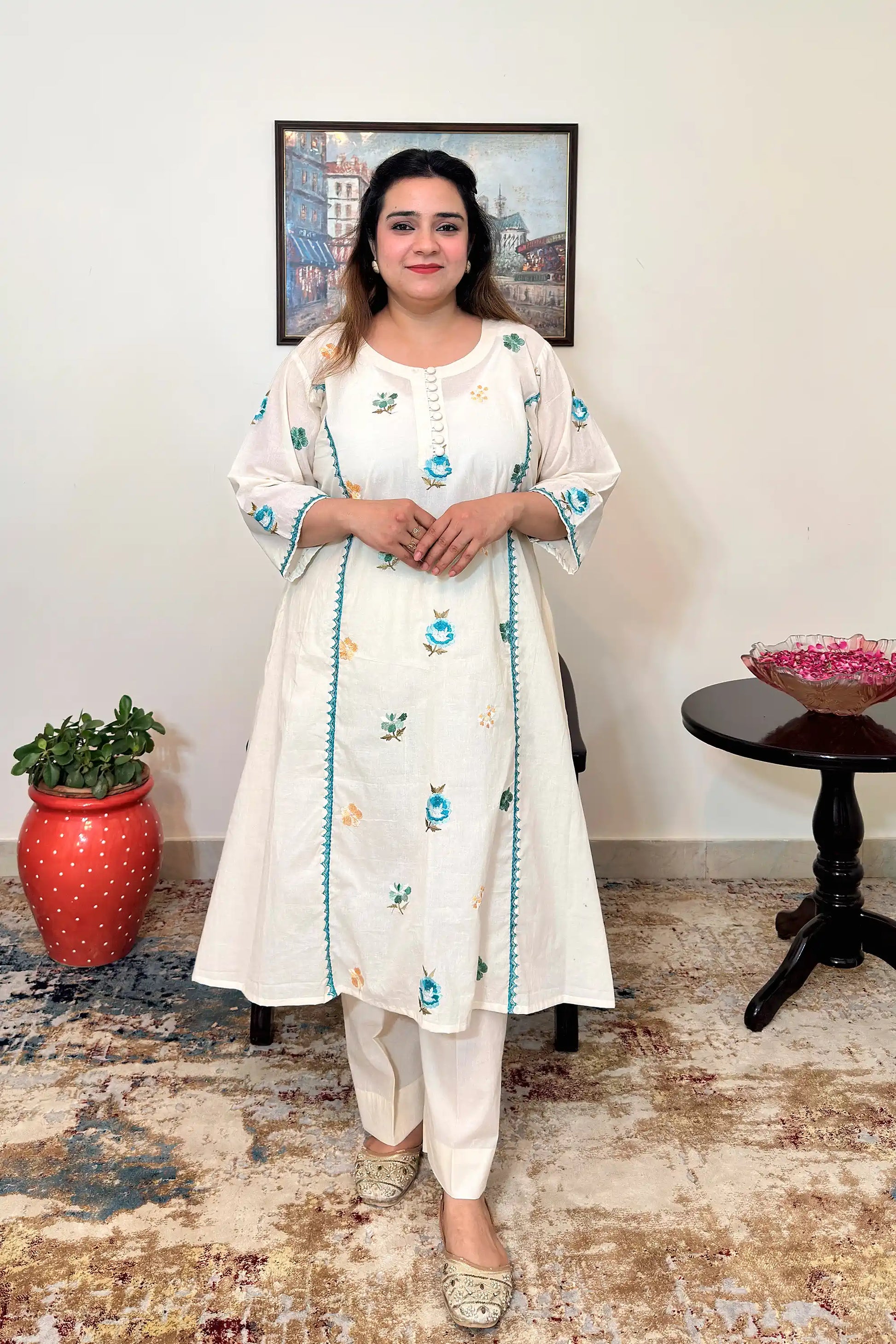 Front view of an off-white cotton frock kurta with multicolour floral resham embroidery and off-white trousers.