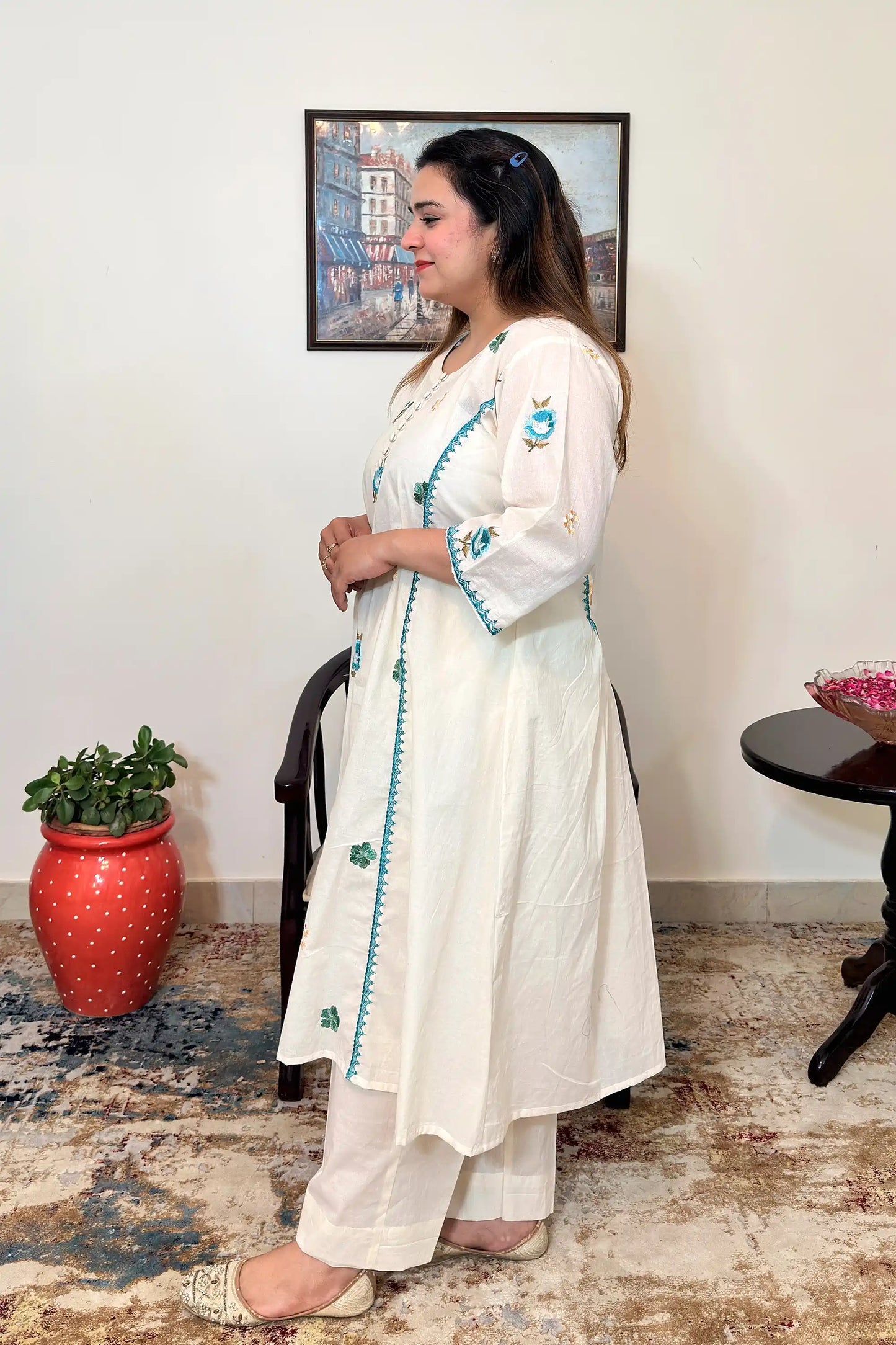 Side view of an off-white cotton frock kurta with multicolour floral resham embroidery, worn with off-white trousers.