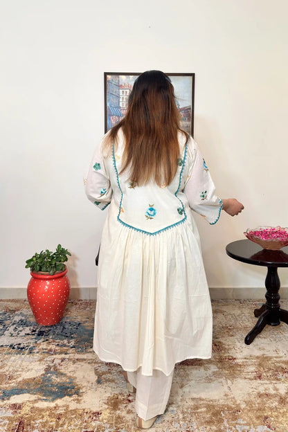 Back view of an off-white cotton frock kurta with multicolour floral resham embroidery on the yoke and sleeves, worn with off-white trousers.