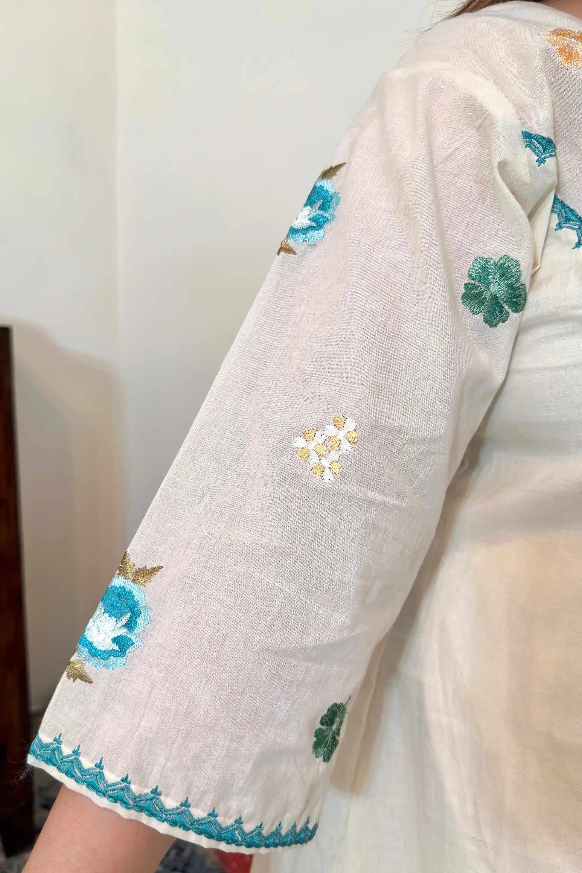 Close-up of the sleeve of an off-white cotton frock kurta showing multicolour floral resham embroidery.