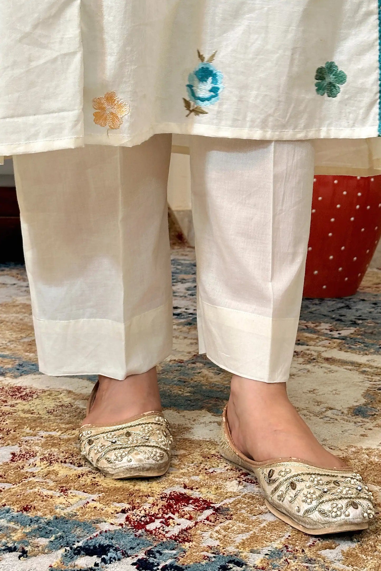 Close-up of the hem of off-white cotton trousers with multicolour floral resham embroidery.