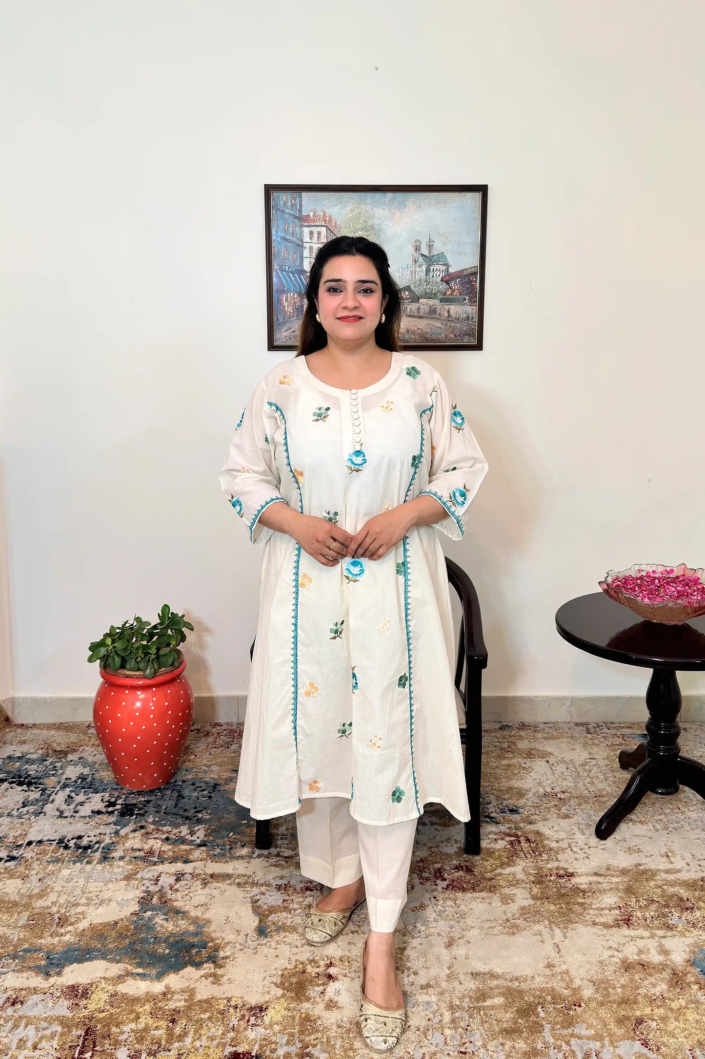Front view of an off-white cotton frock kurta with multicolour floral resham embroidery and off-white trousers.