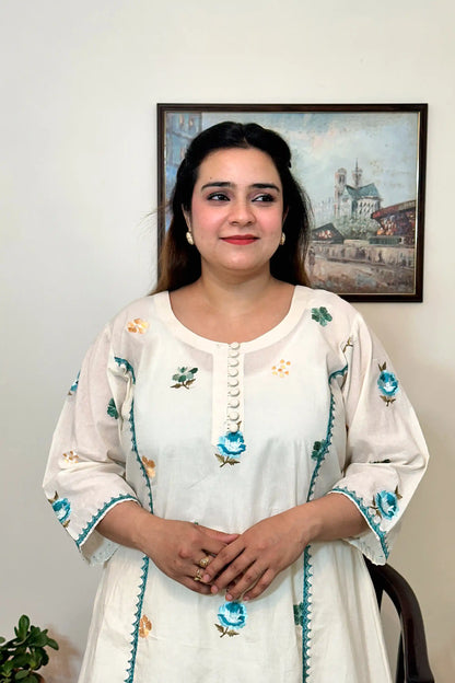 Front close-up of an off-white cotton frock kurta showing multicolour floral resham embroidery along the button placket and sleeves.
