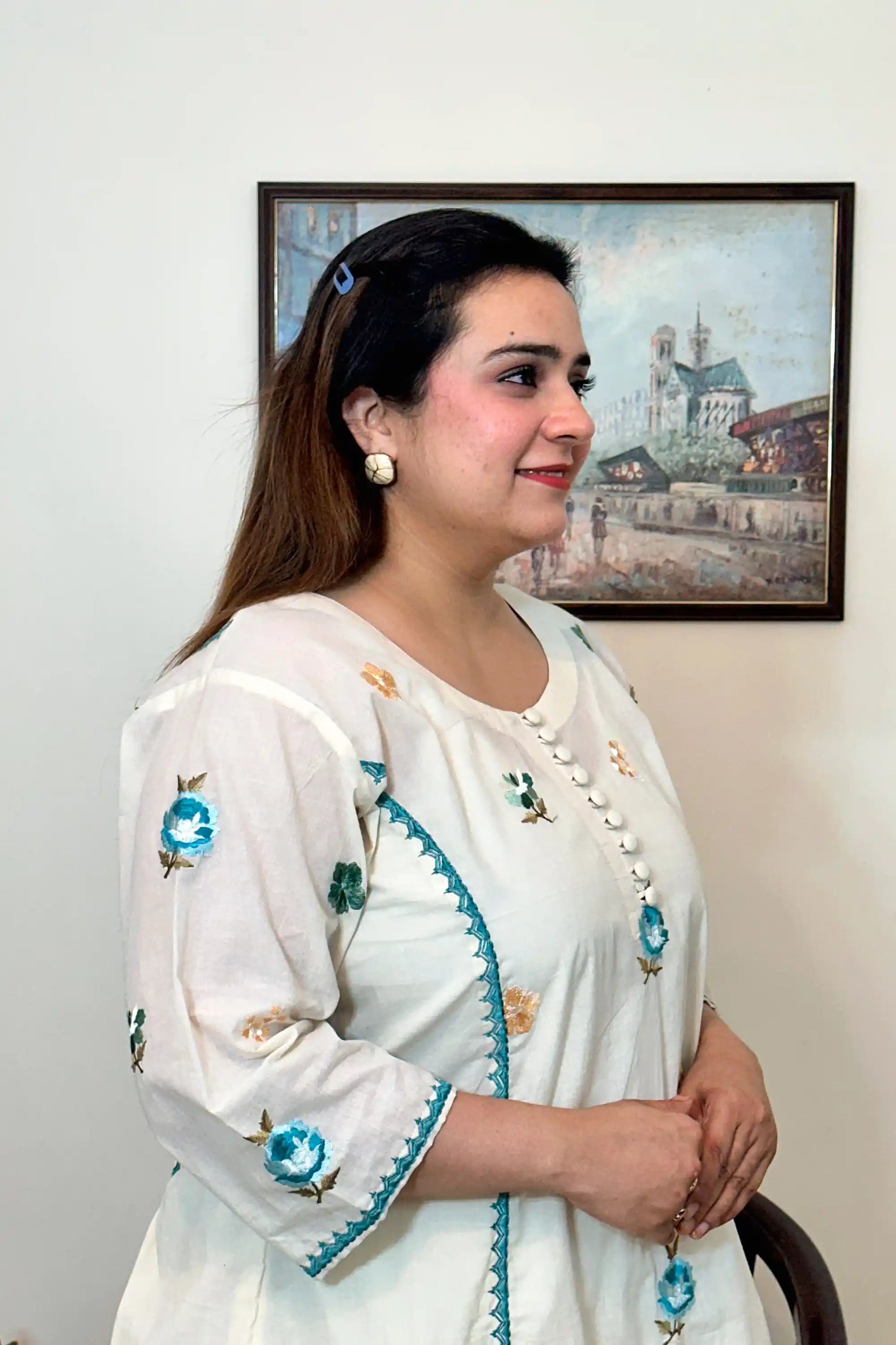 Side close-up of an off-white cotton frock kurta showing multicolour floral resham embroidery along the button placket and sleeve.