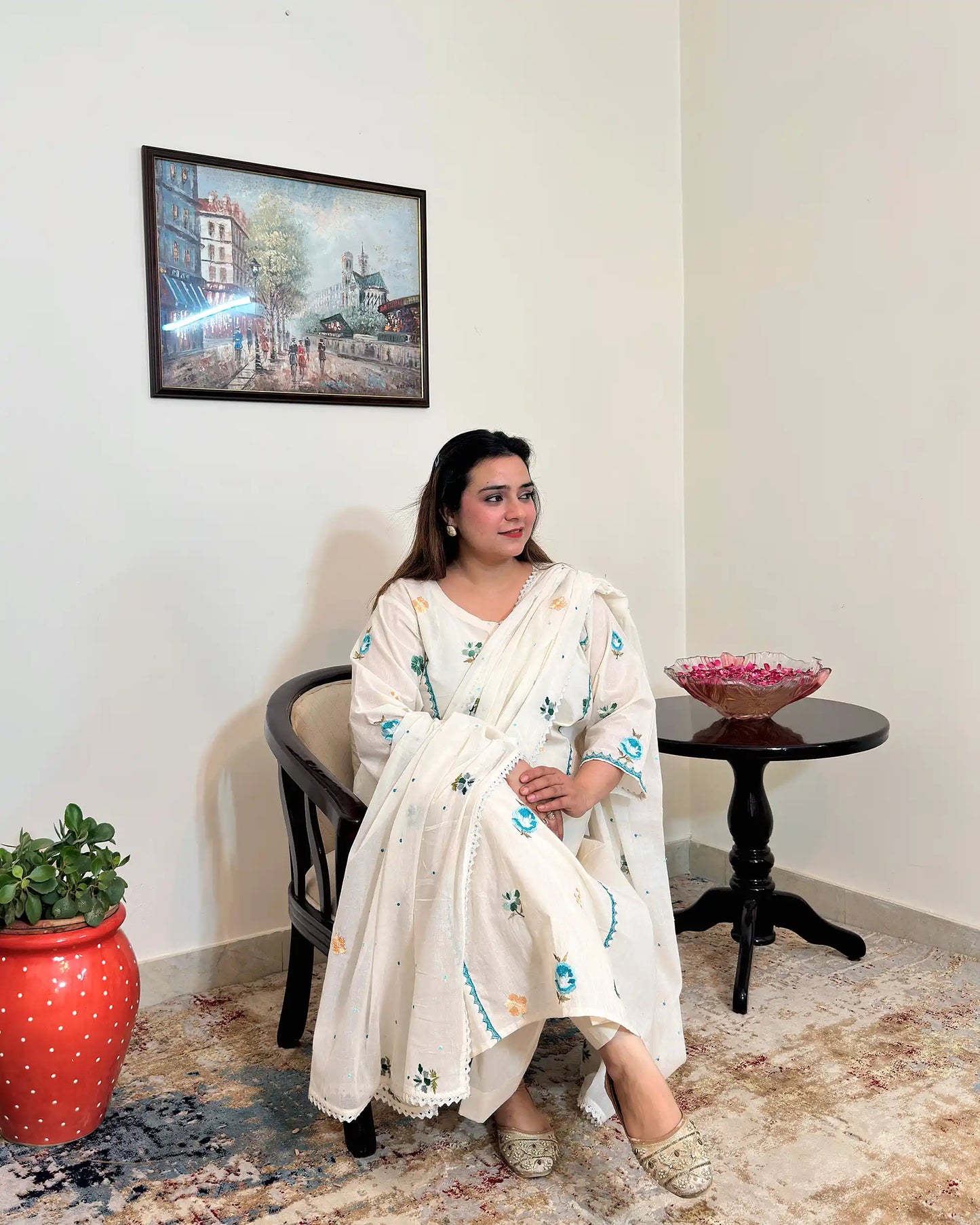 Front seated view of an off-white cotton frock kurta and dupatta with multicolour floral resham embroidery, worn with off-white trousers.
