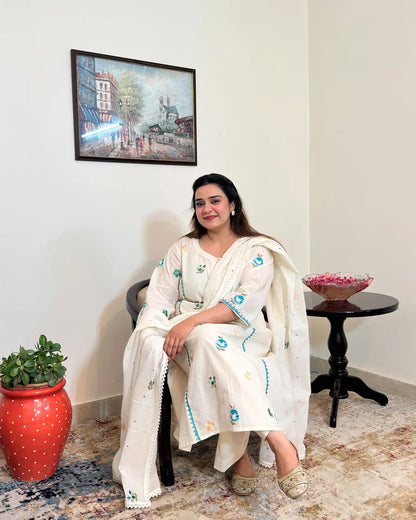 Front seated view of an off-white cotton frock kurta and dupatta with multicolour floral resham embroidery, worn with off-white trousers.