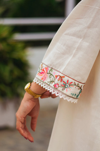 An Indian woman wearing an off-white asymmetric kurta set, her hand gently resting on her side