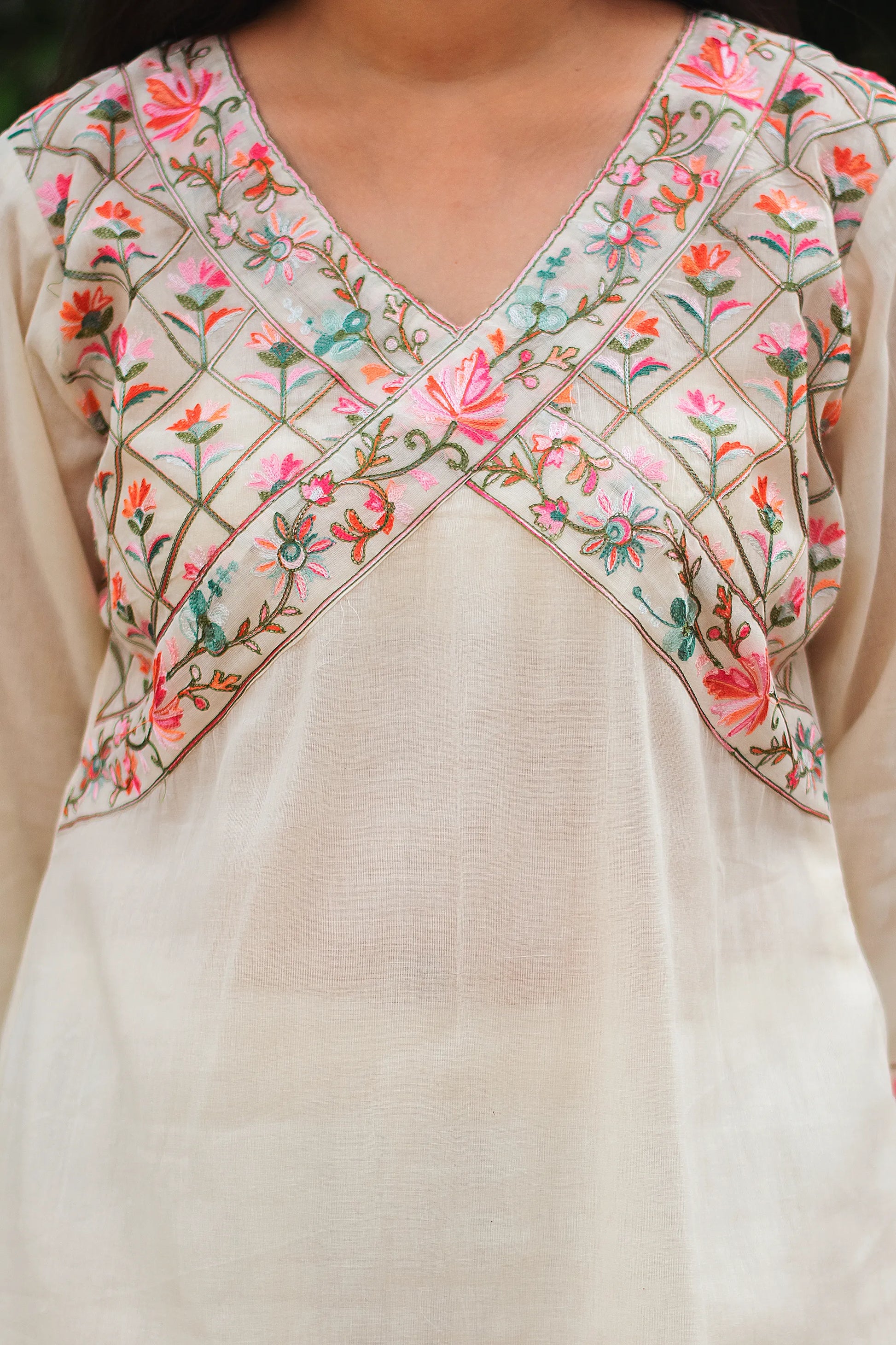 An Indian woman wearing an off-white asymmetric kurta set, showcasing the intricate neckline detailing