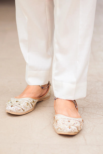 Close-up of off-white trousers featuring intricate Kashmiri embroidery, worn with matching sandals